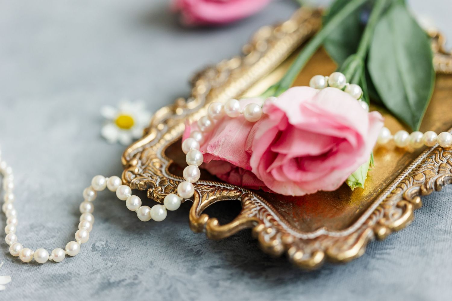 Pink rose and pearl necklace on a vintage gold tray with a daisy, elegant wedding flat lay.