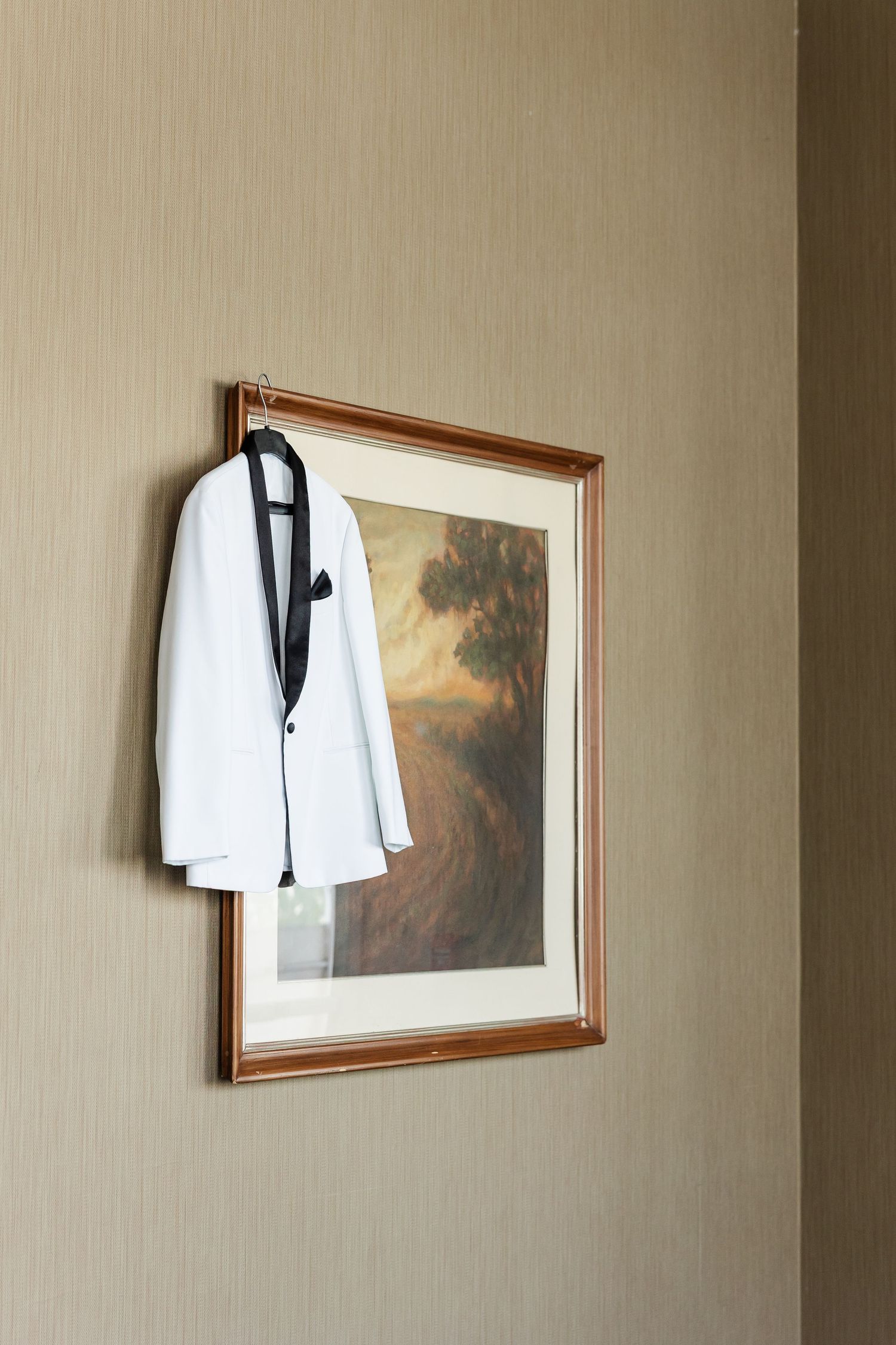White tuxedo jacket with black lapels hangs on framed painting in hotel room.
