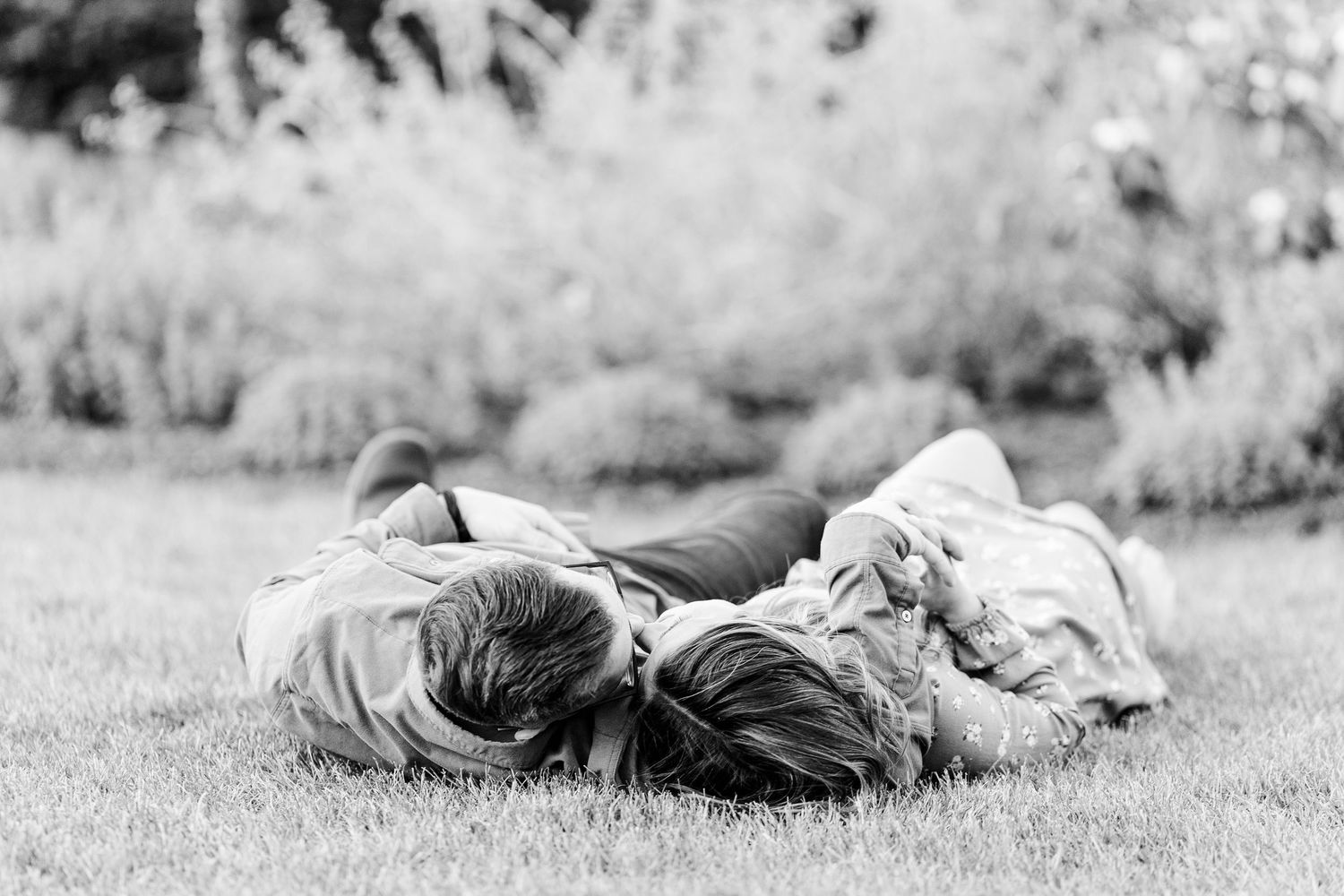 Black and white engagement photo of a couple lying in the grass at Cantigny Park.