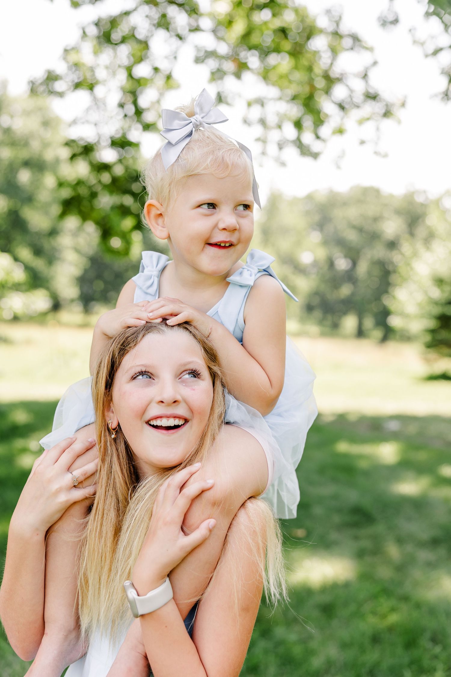 Older sister carrying her baby sister on her shoulders during a playful summer family session in Crystal Lake, IL.
