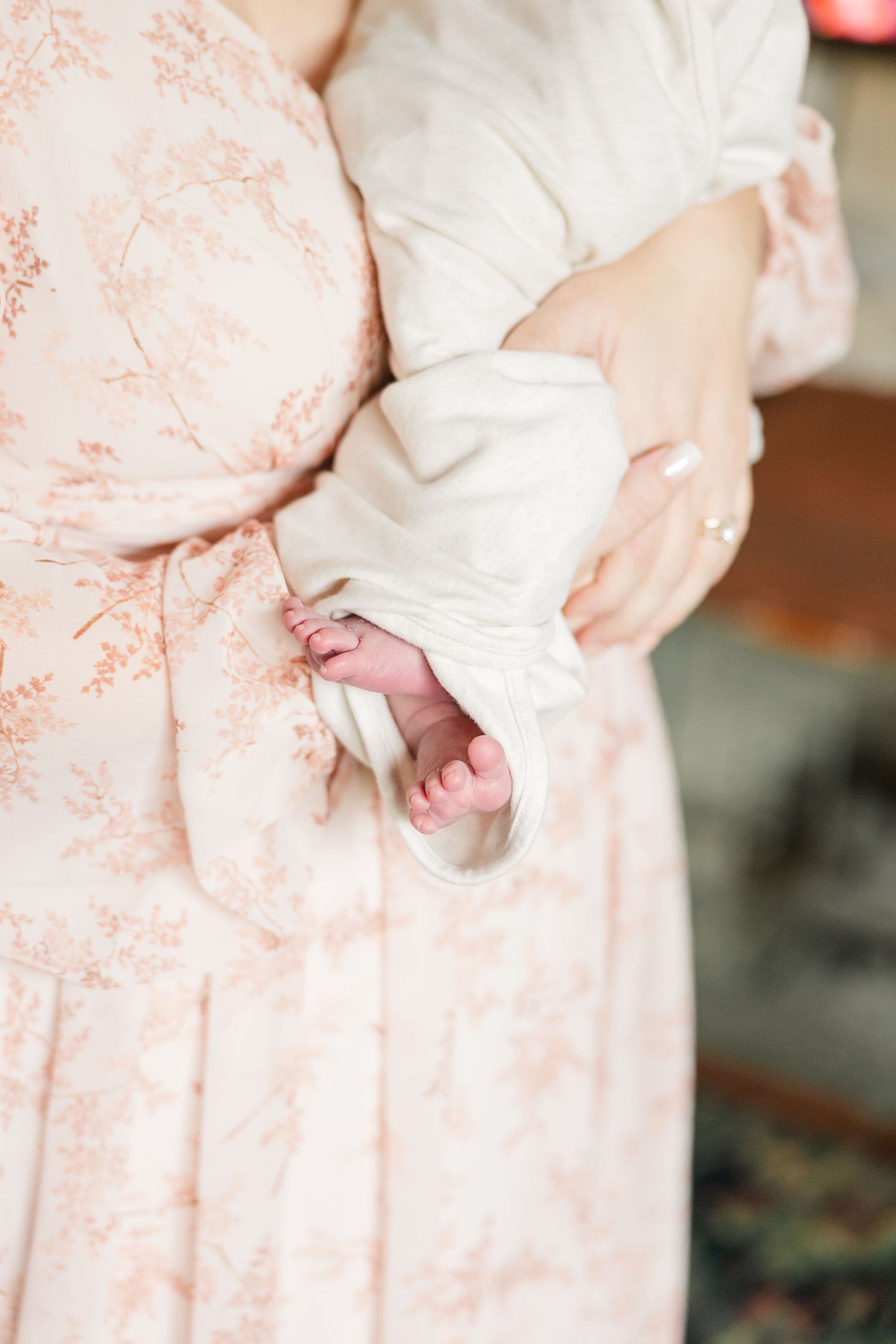 Close-up of newborn baby's tiny feet peeking from white swaddle held by mother in pink dress.