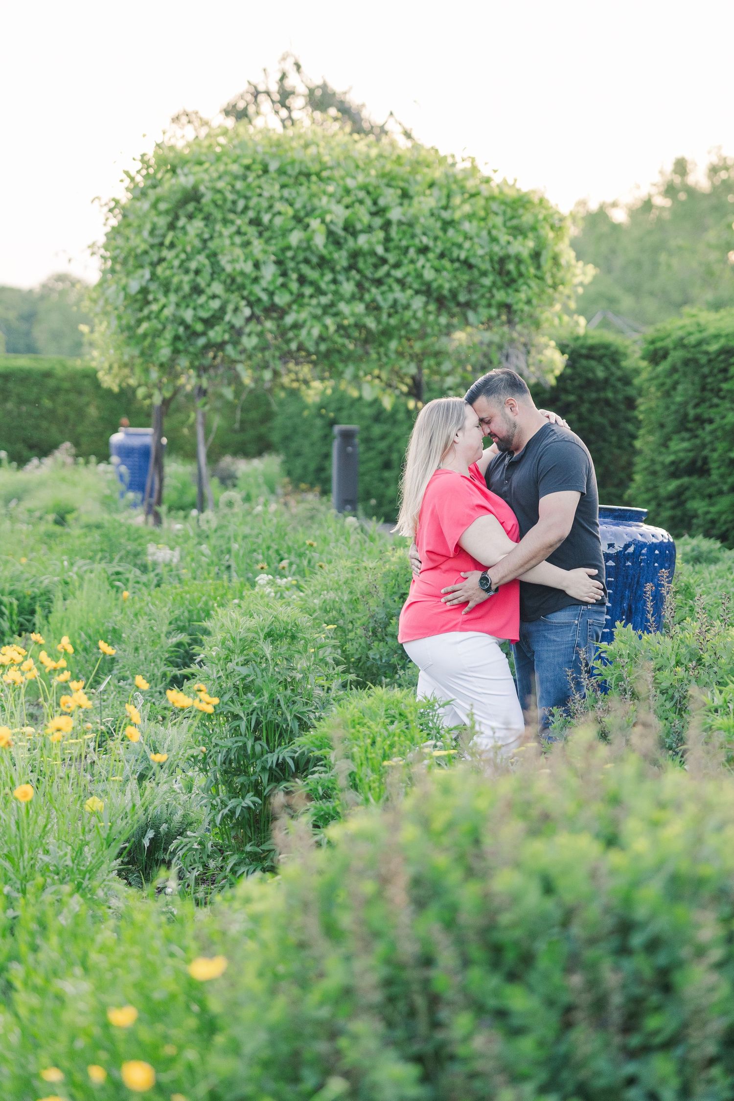 Couple embracing among yellow flowers and green shrubs in a landscaped garden.