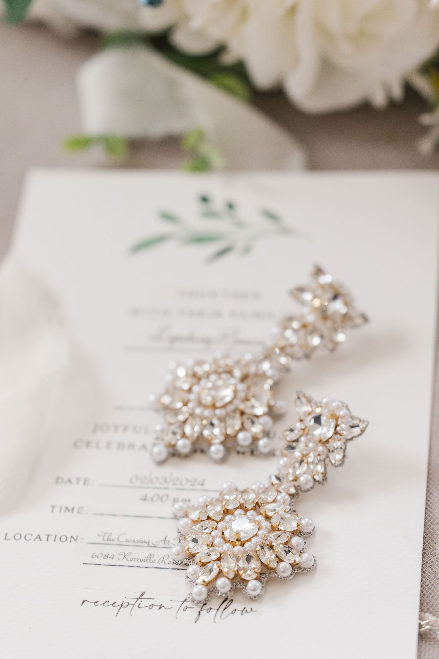 Crystal and pearl chandelier wedding earrings displayed on invitation with floral design.
