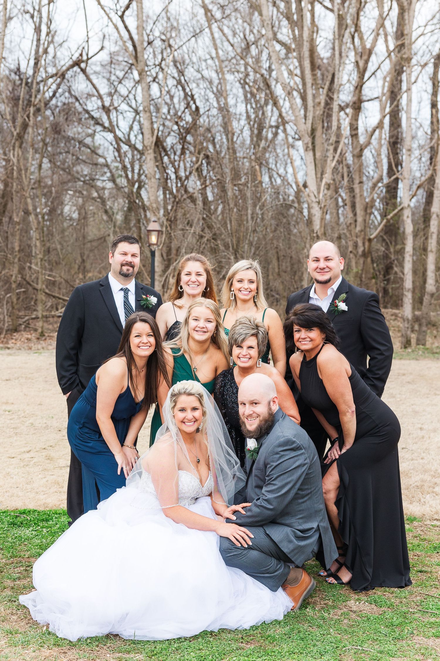 Wedding party arranged in casual group pose outdoors with bridesmaids in elegant black gowns.