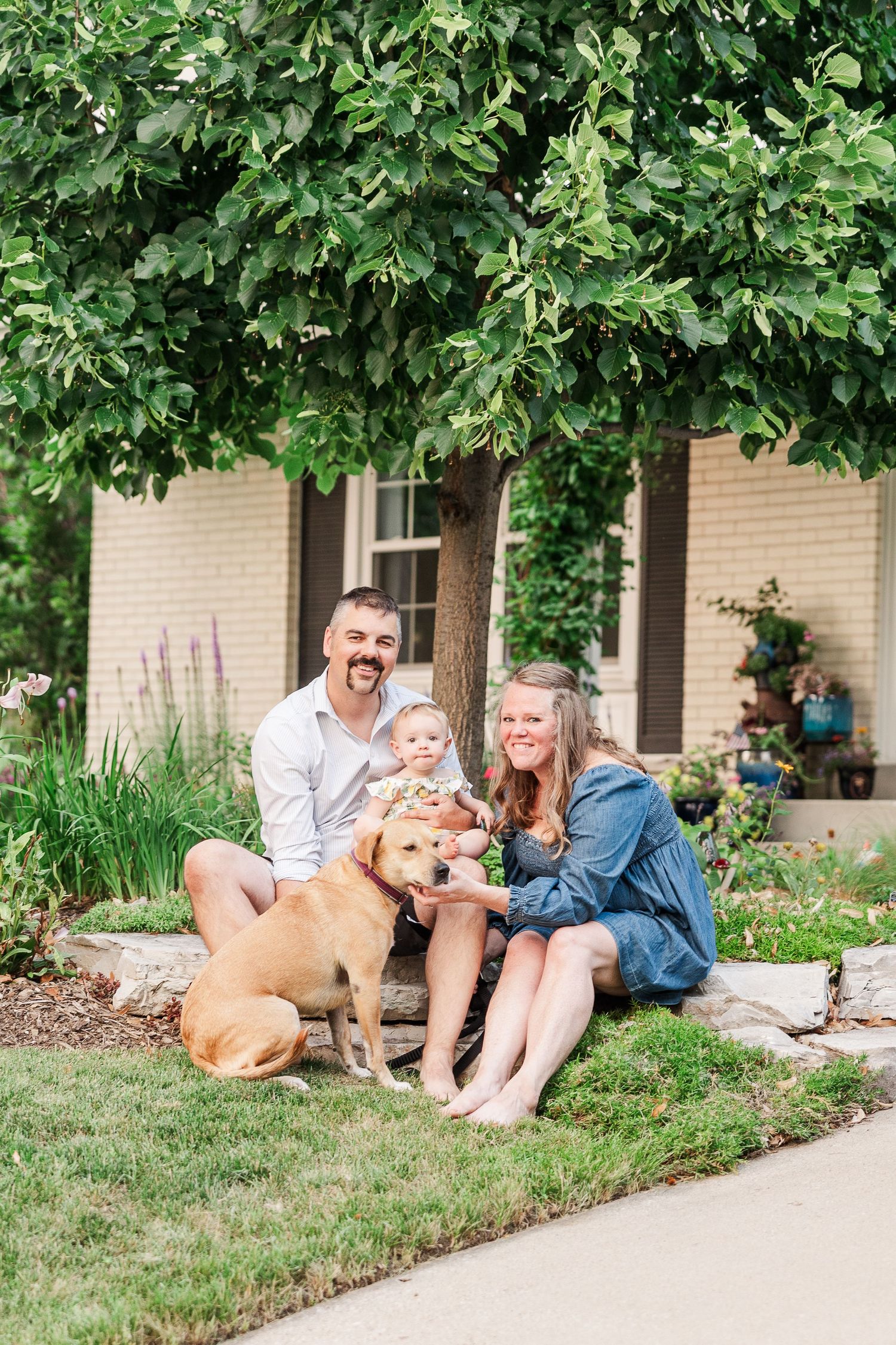 Family and their golden dog posing together in front of a house with lush landscaping.