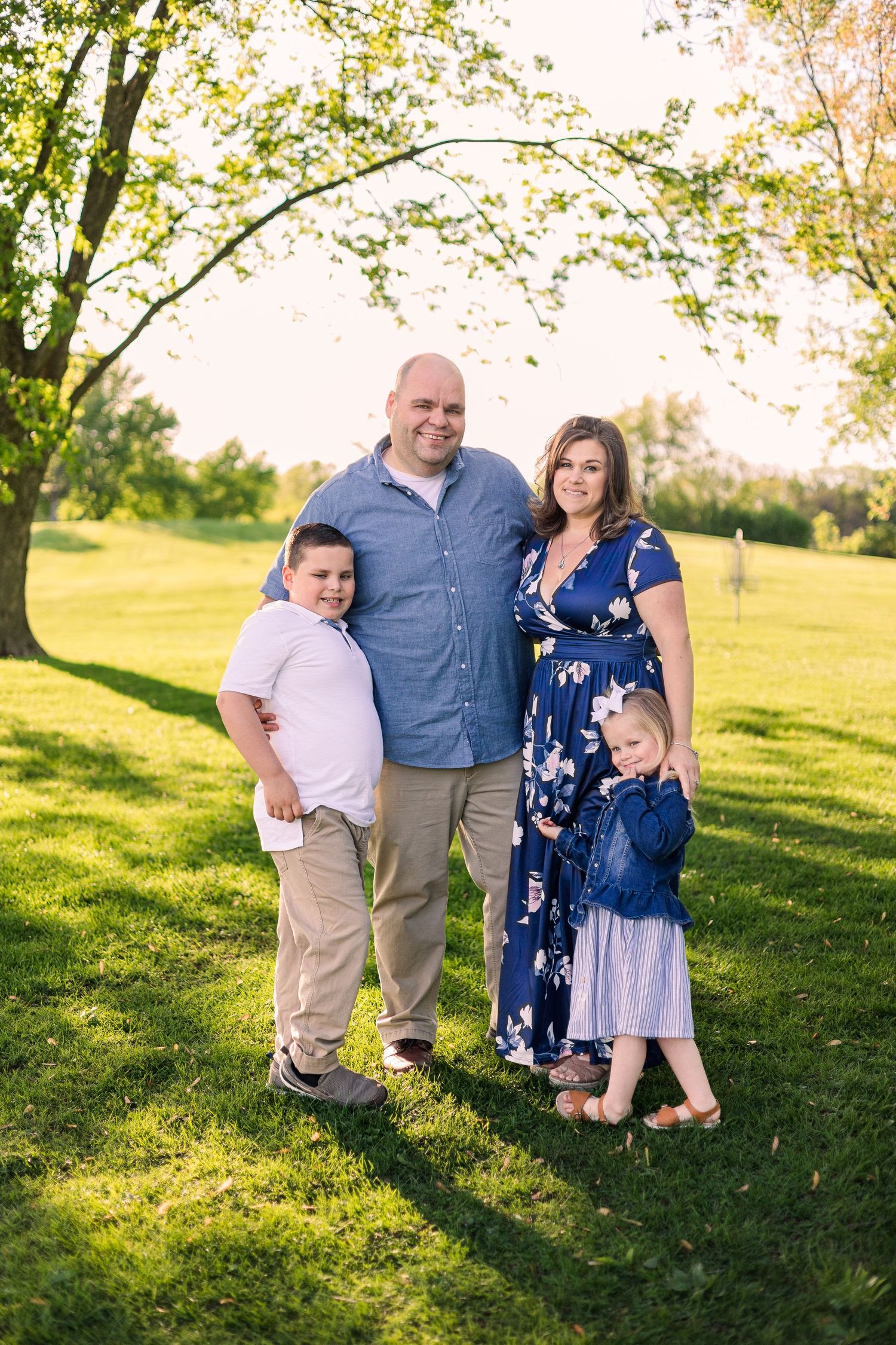 Family portrait taken in a park during golden hour with trees and grass in the background.