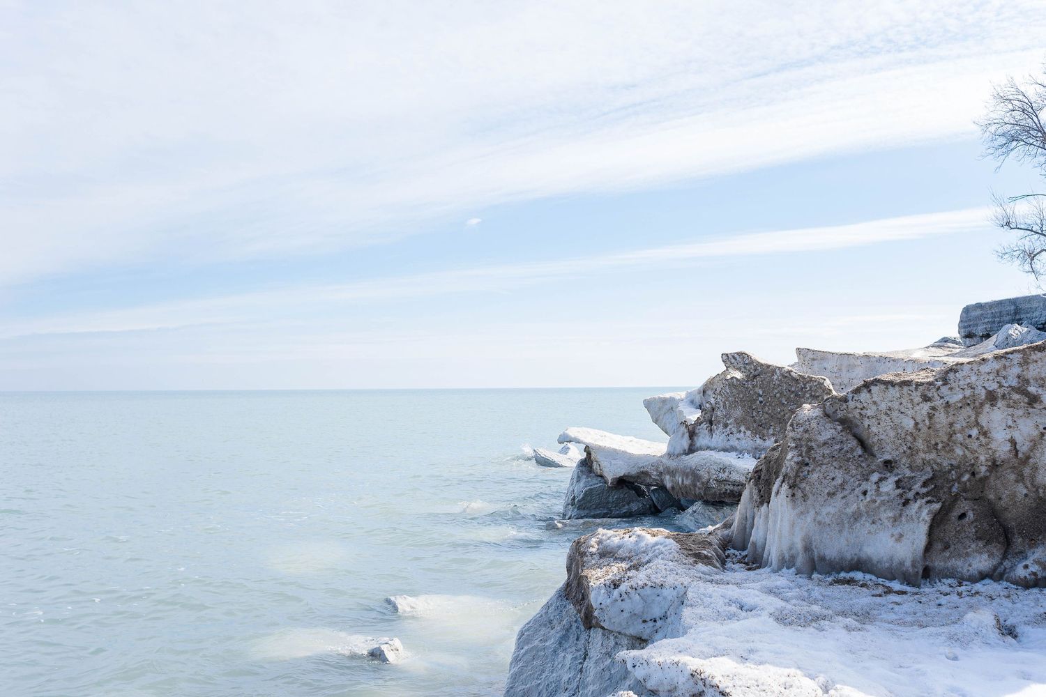 Snow-covered rocky cliffs overlooking a frozen lake under wispy clouds.