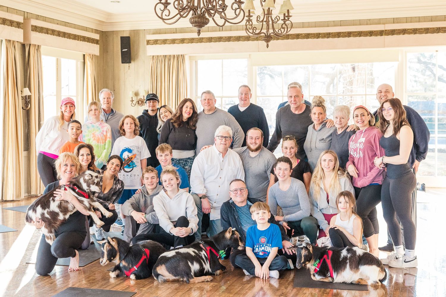 A large group photo of people and pets gathered in an elegant room with chandeliers.