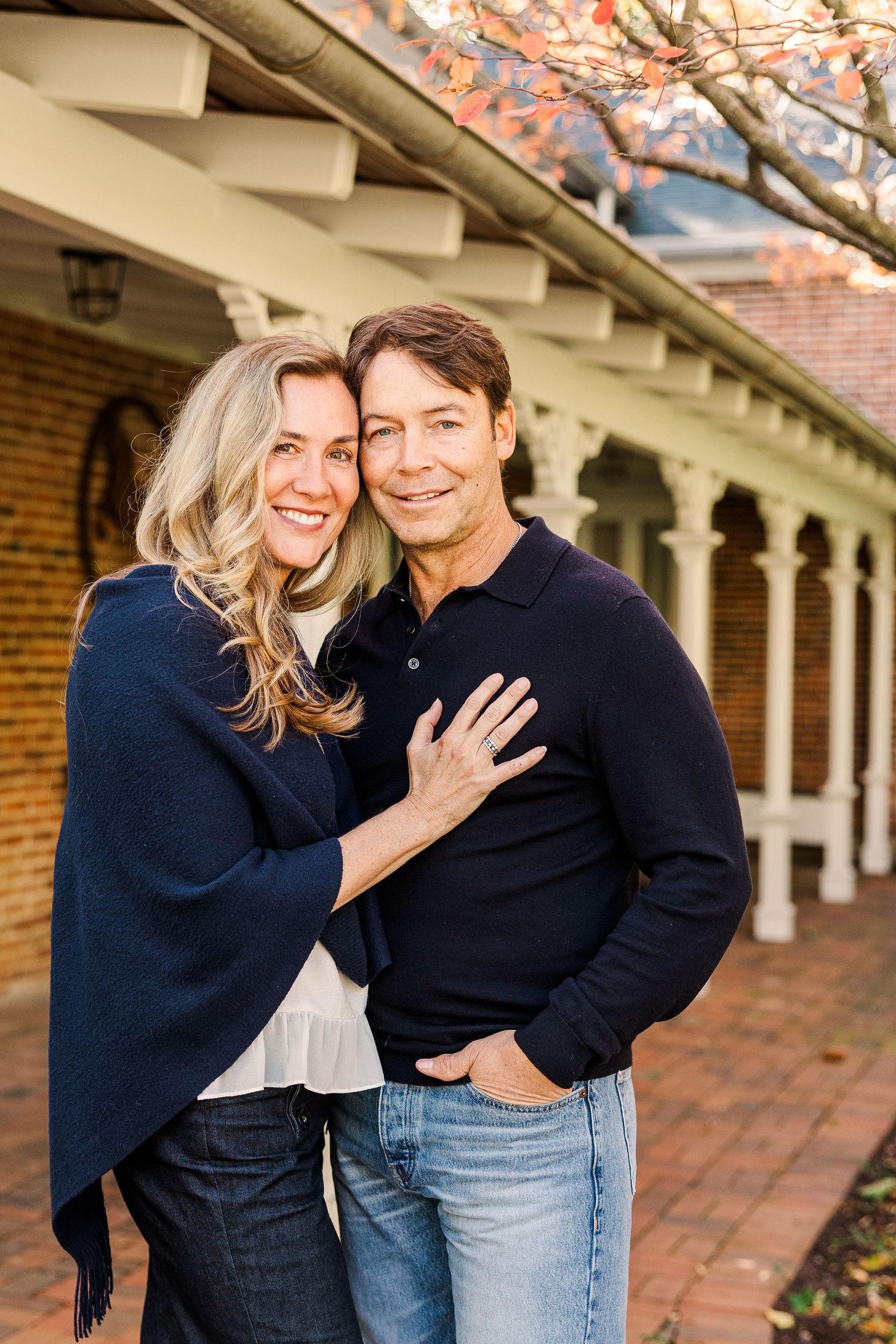 A couple shares an intimate moment while standing on a brick terrace with white columns.