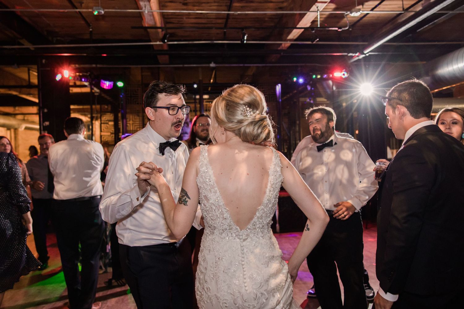 Wedding celebration on dance floor with party lights and industrial ceiling.