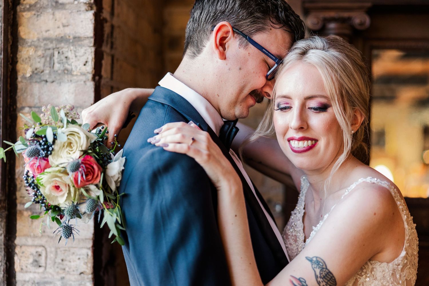 A tender embrace captured between newlyweds in front of exposed brick and natural lighting.