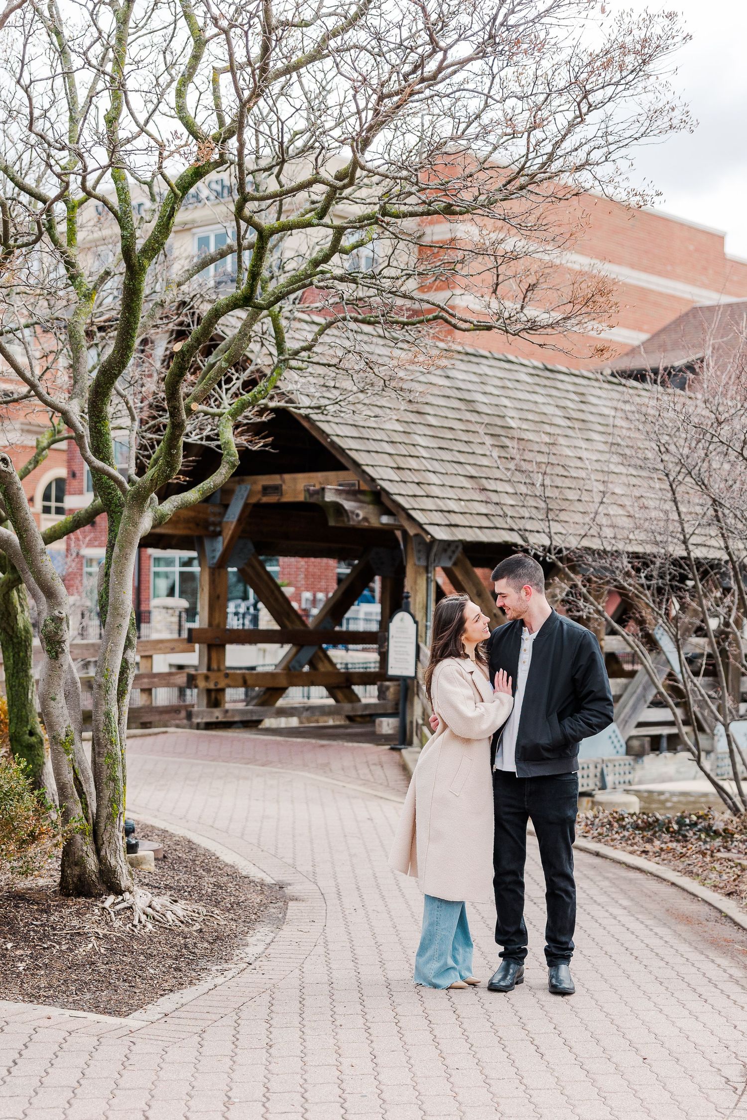 A romantic moment captured on a brick pathway near a rustic wooden gazebo and bare winter trees.