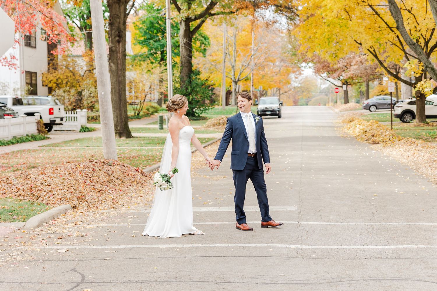 Couple walking on leaf-covered street during autumn wedding photoshoot.