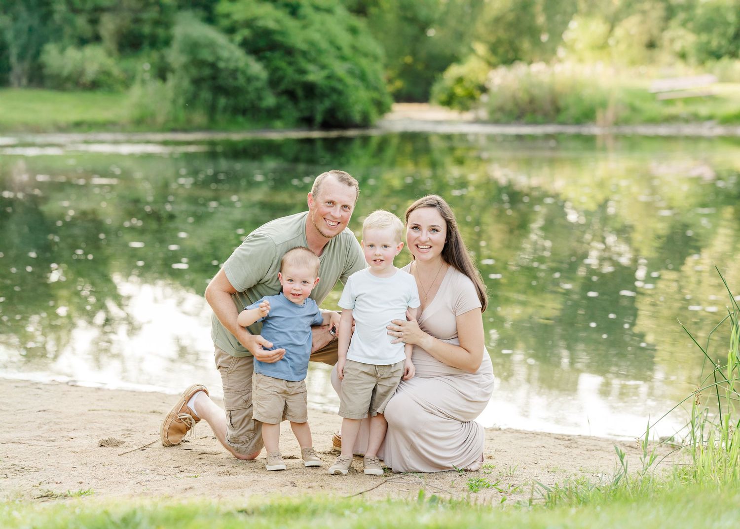 Family relaxes and enjoys quality time together by a serene pond surrounded by lush greenery on a sunny day.