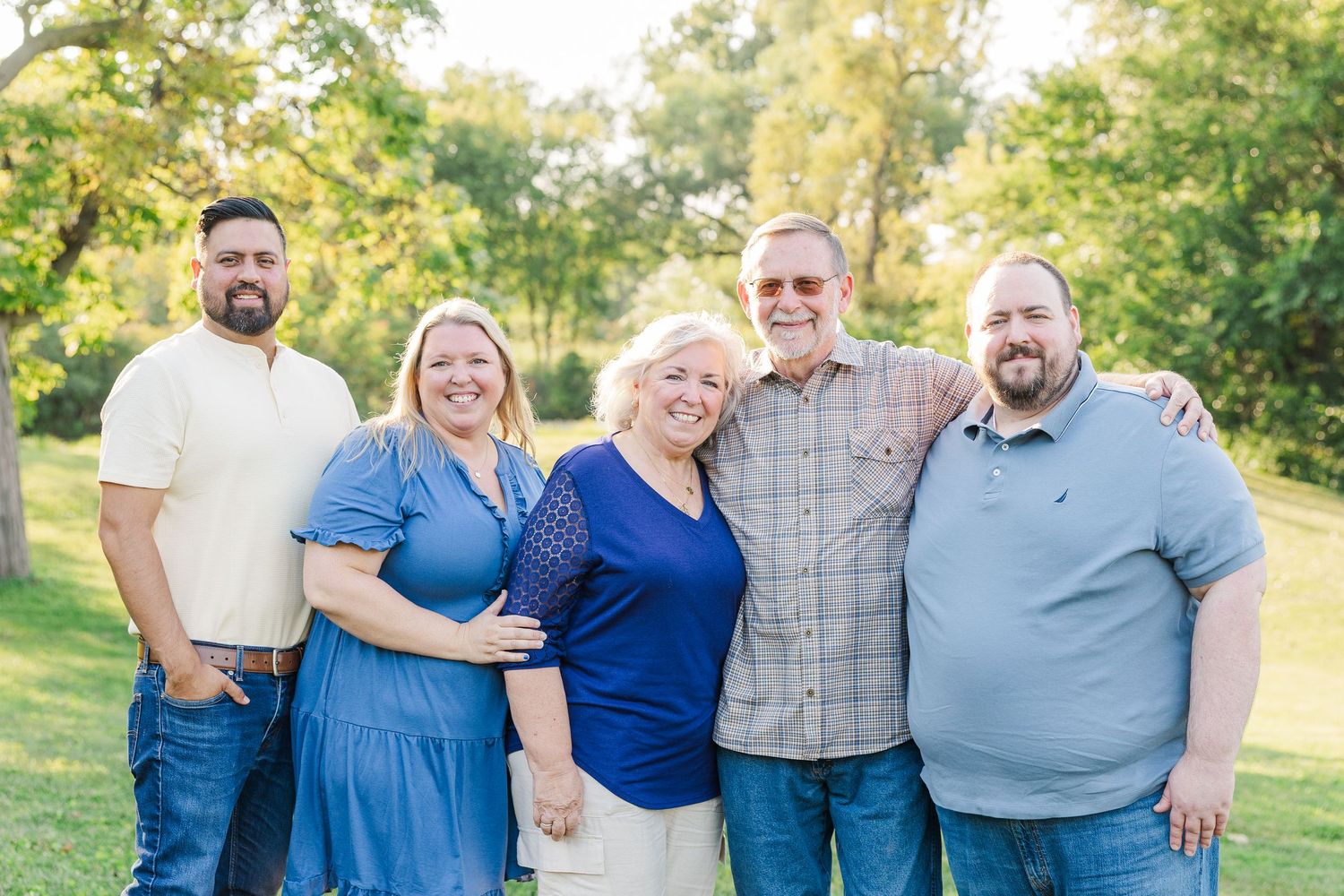 A group wearing coordinated blue and grey outfits poses together outdoors in a sunny garden setting.Sorg family portraits at Shamrock Hills