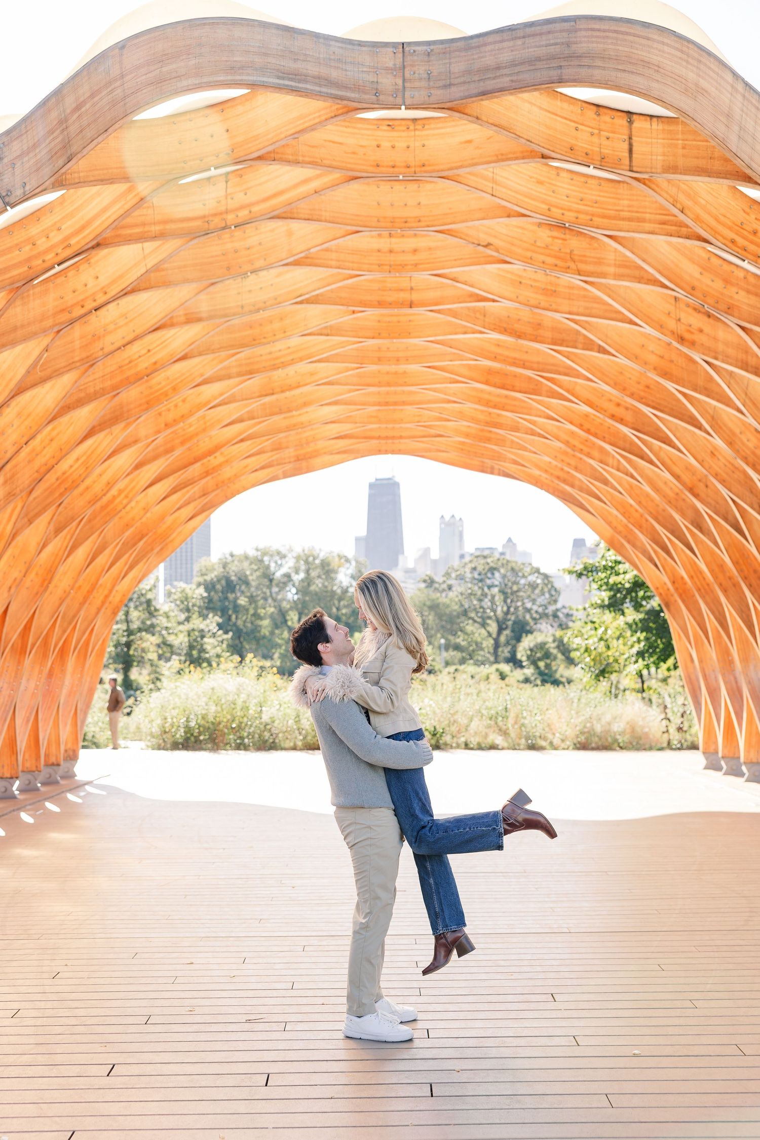 Man lifting woman in a joyful embrace under a stunning orange wooden arch structure in Chicago park.