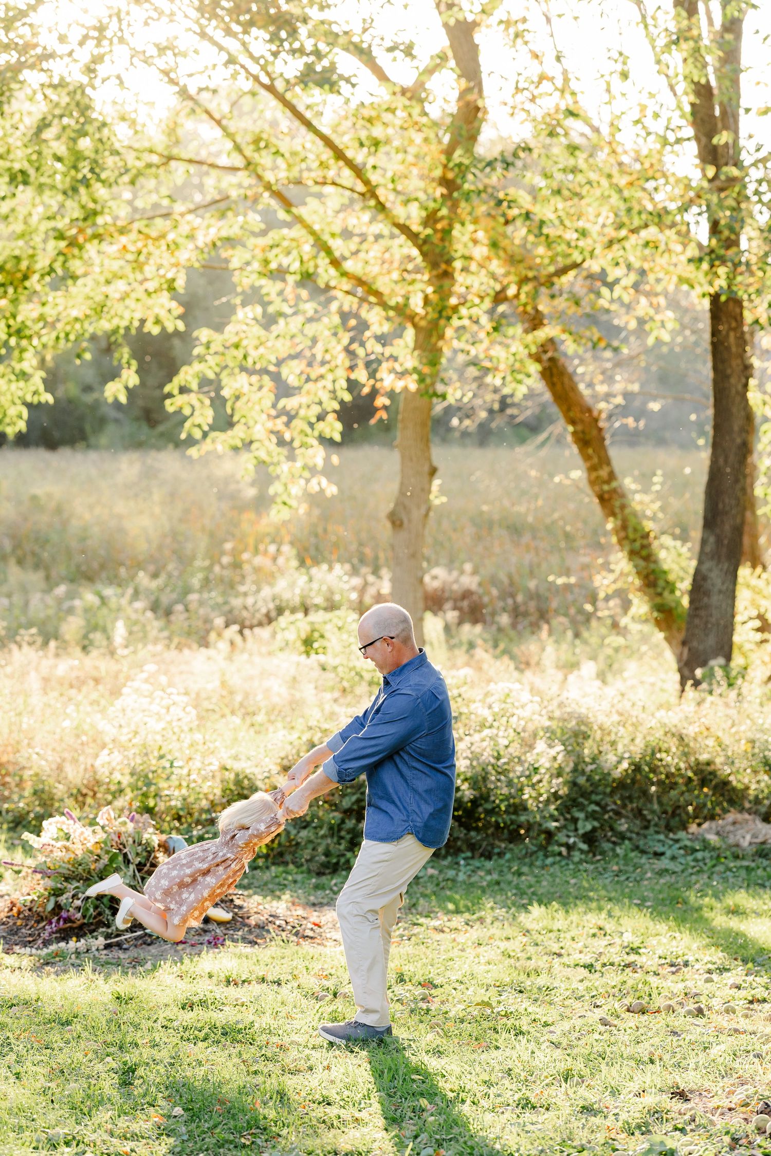 Dad swinging his young daughter by her hands in their sunlit backyard in St. Charles, IL.