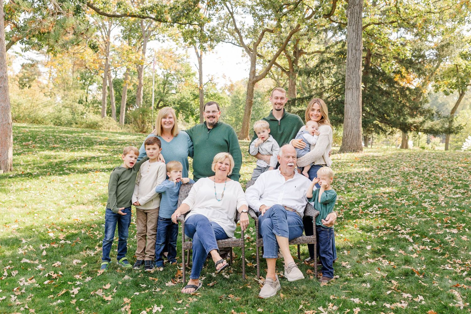 Multi-generational family portrait outdoors in autumn park with grandparents seated center surrounded by children and grandchildren.