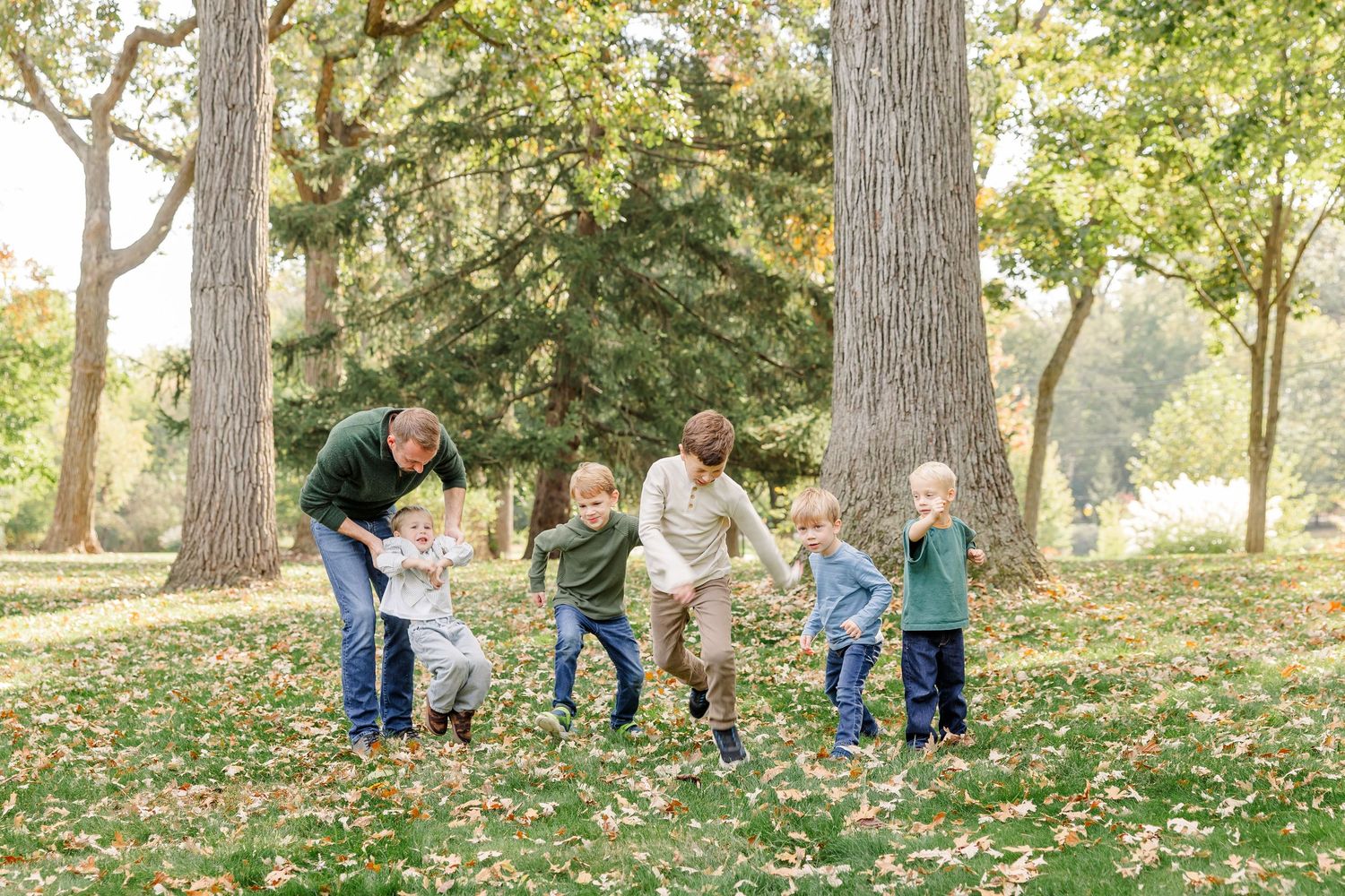 Family with four boys playing outdoors in a park surrounded by tall trees and autumn leaves.