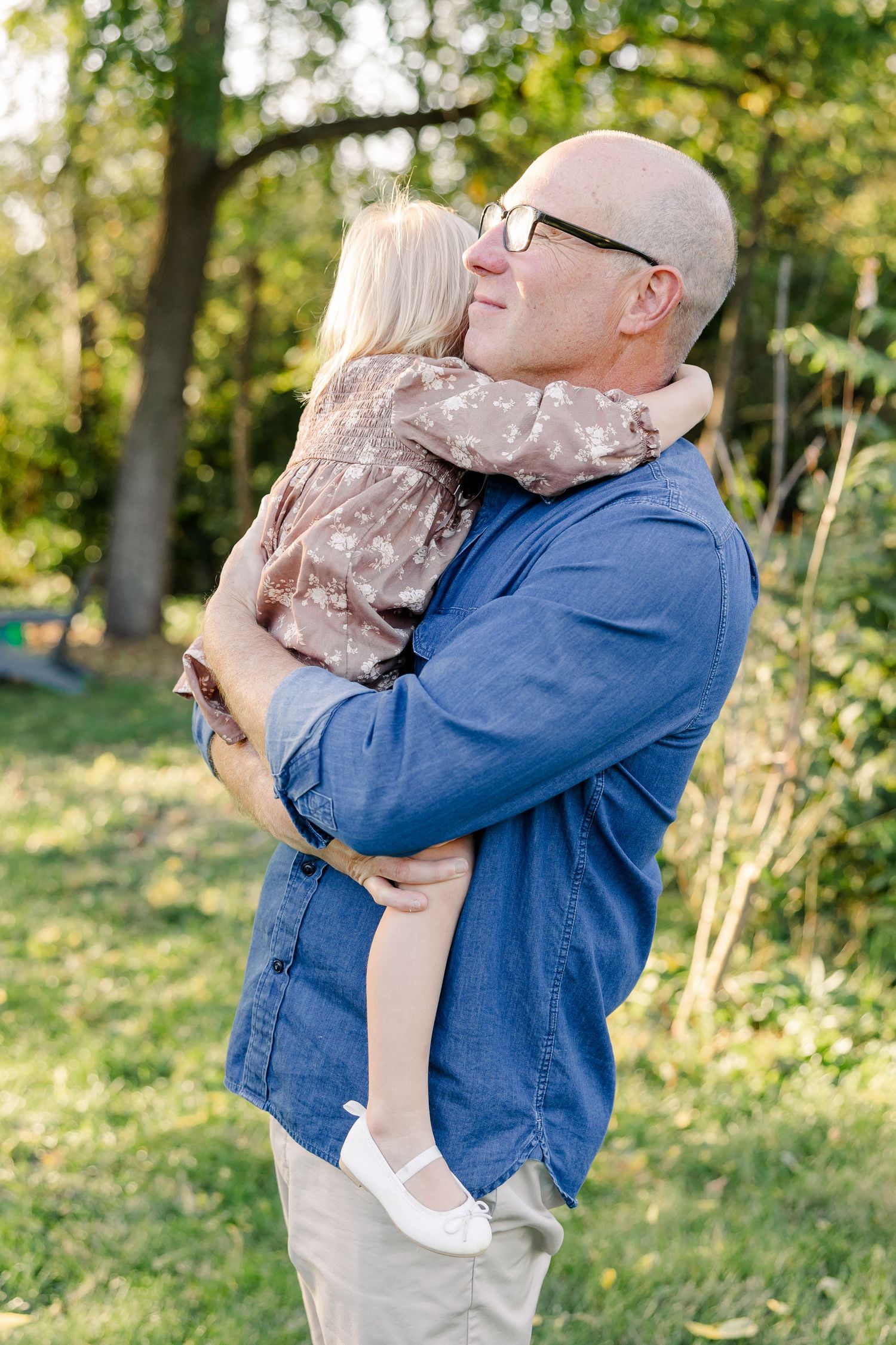 Dad holding his youngest daughter as she hugs his neck during backyard family photos in St. Charles, IL.