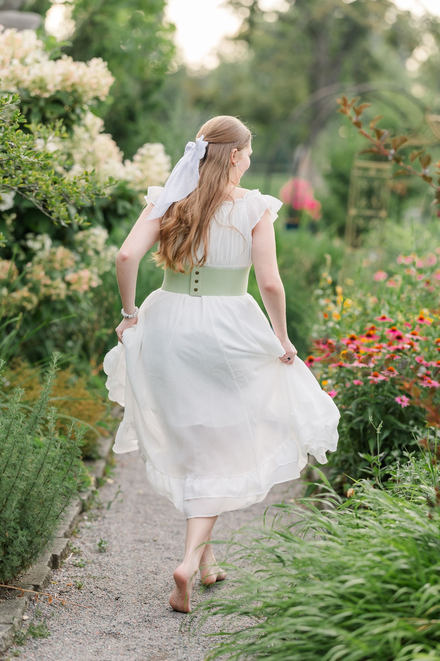 Samantha walks along a flower-lined path in a flowing white dress during her Cantigny Park senior portraits.