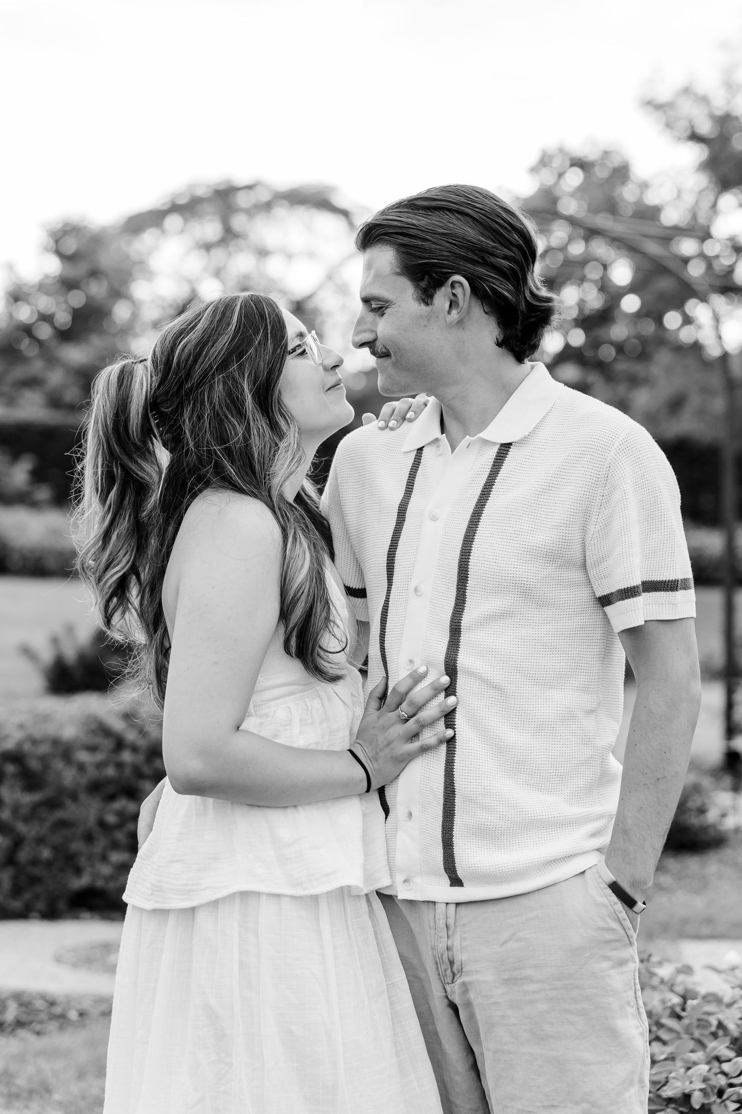 Black and white photo of romantic couple smiling at each other in outdoor garden setting.