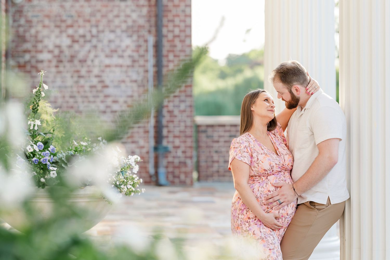 Romantic maternity photo of expecting parents by flowers and brick architecture at Cantigny Park in Wheaton
