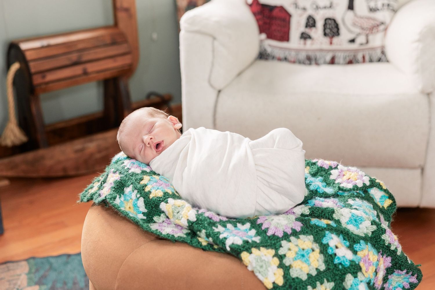 A swaddled newborn baby sleeps peacefully on a colorful crocheted floral blanket.