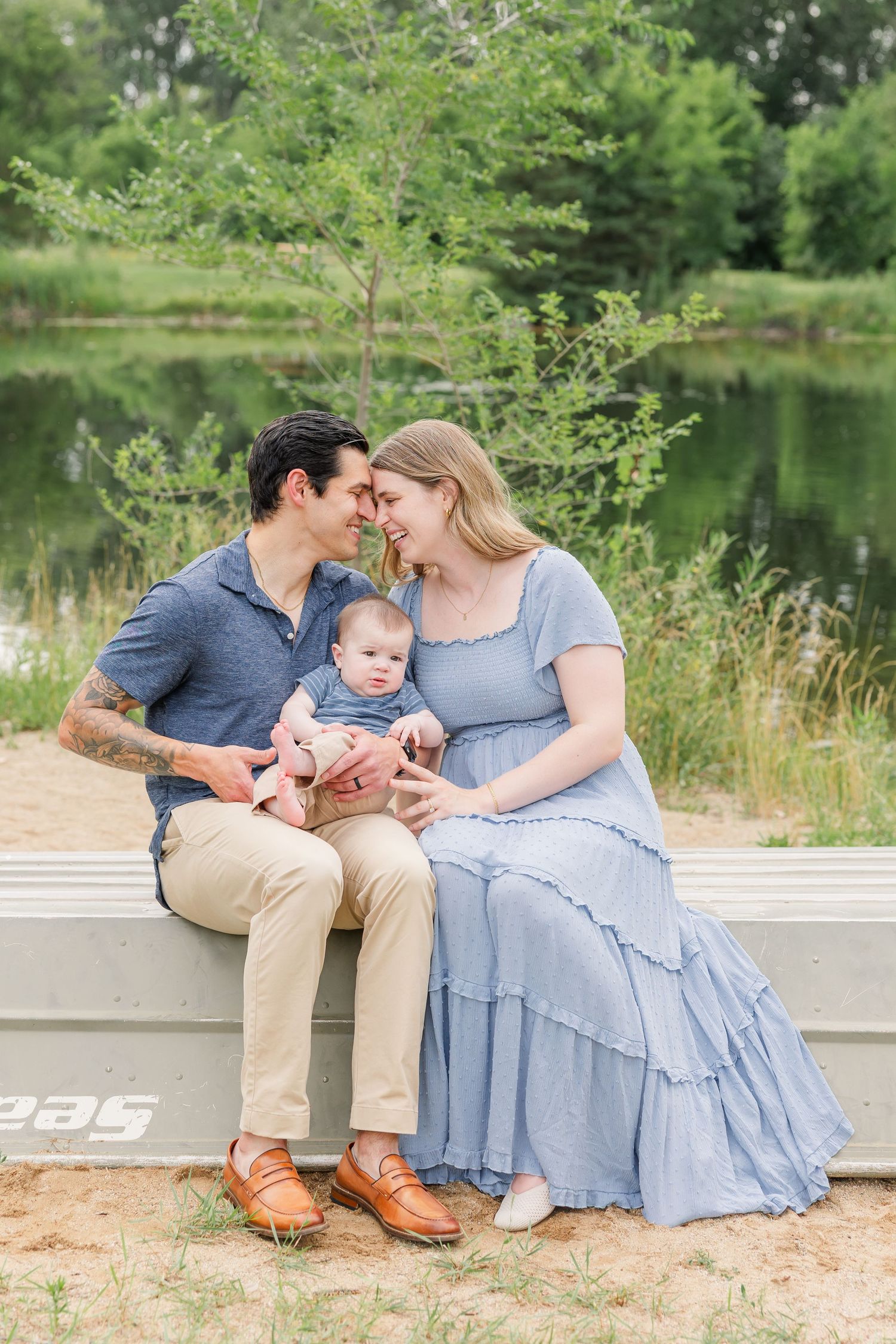 Young couple with baby sitting on bench by a pond, sharing a tender moment together.