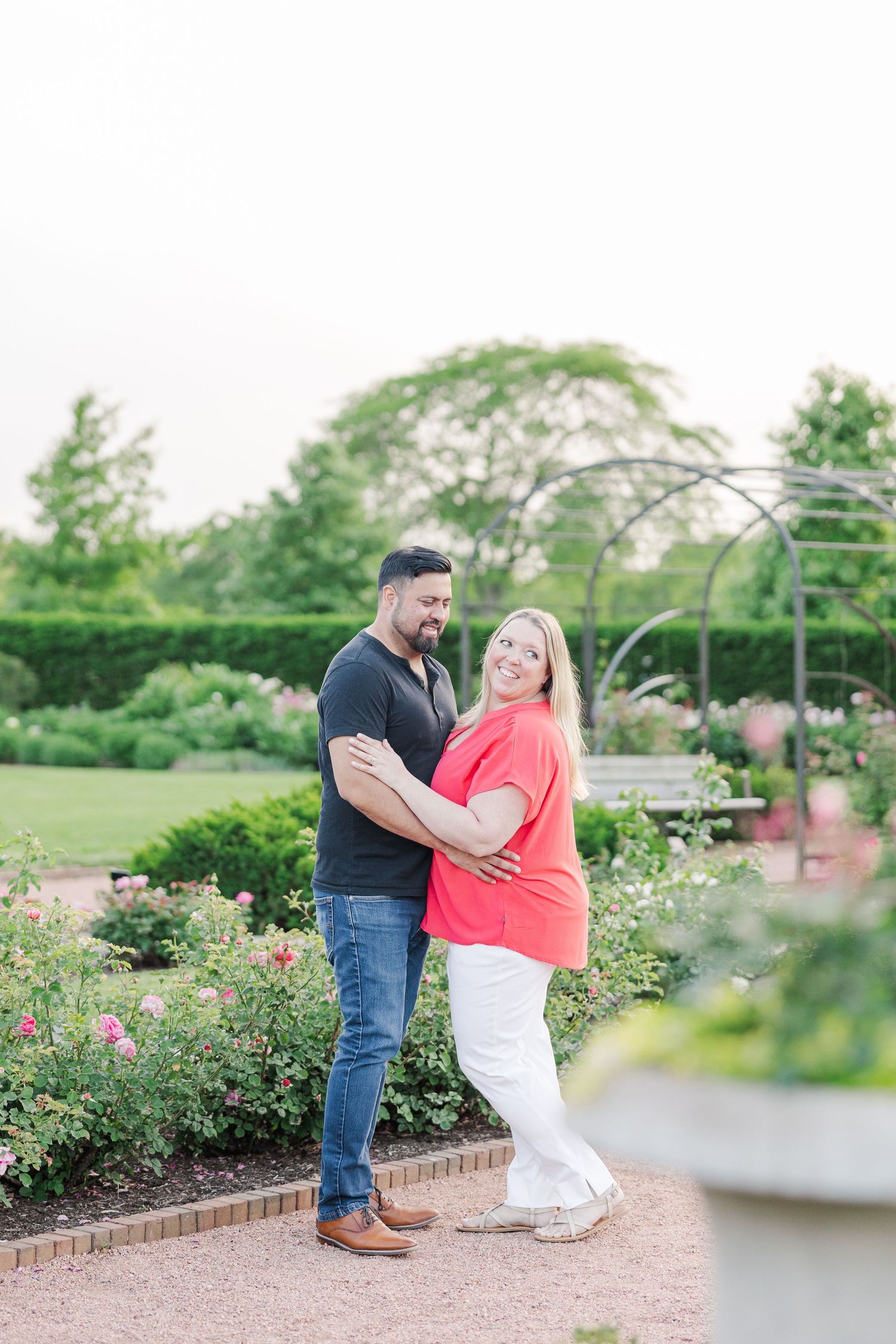 Couple standing together on a brick pathway in a blooming rose garden.