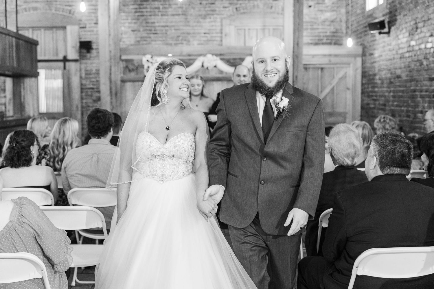 A wedding ceremony exit captured in black and white inside a rustic venue with brick walls.