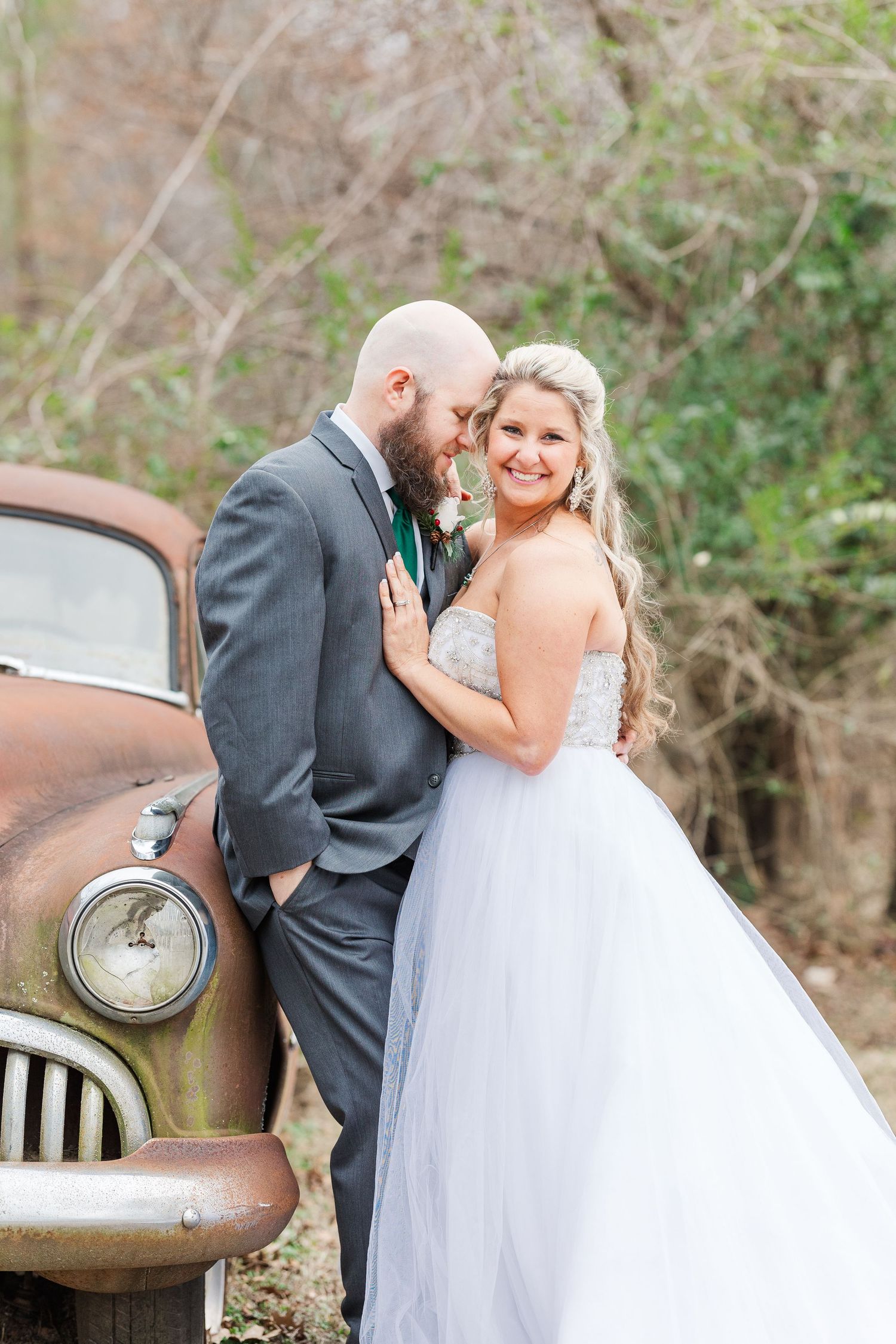 Elegant wedding couple shares intimate moment beside vintage car with rustic patina.