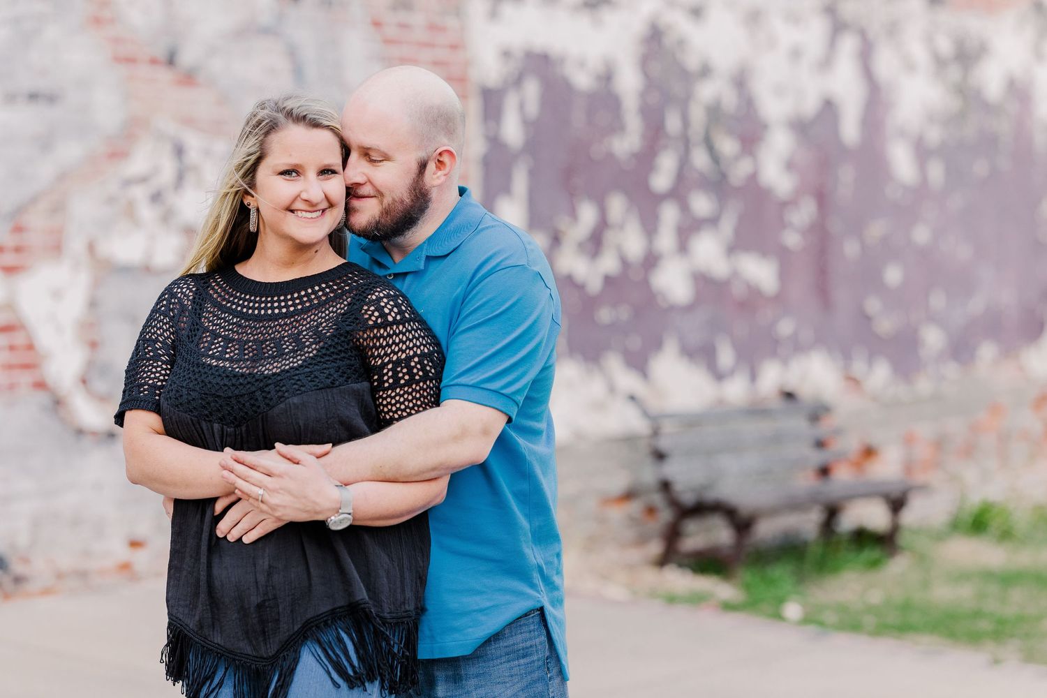 A couple poses together against a weathered wall during an outdoor photoshoot.