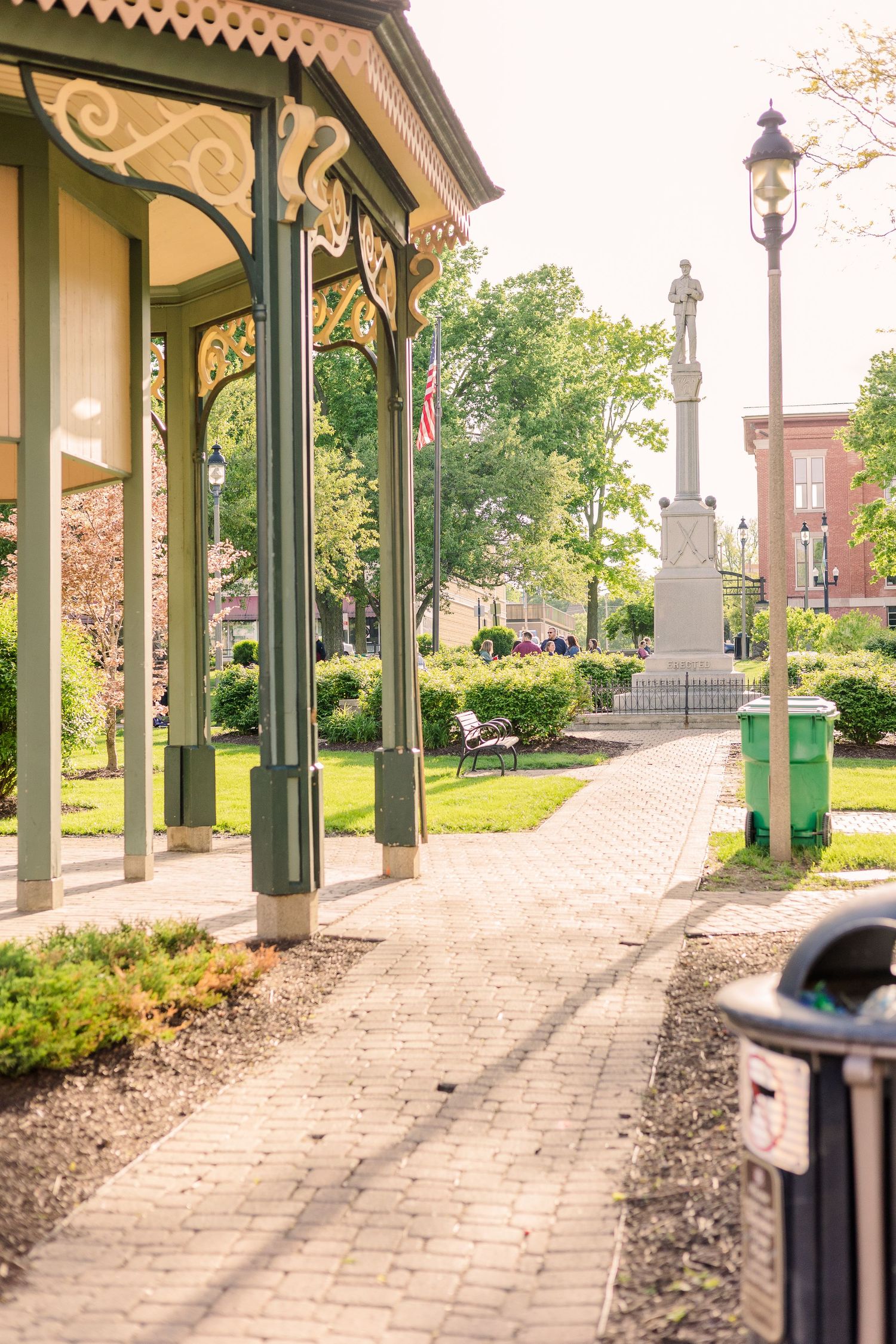 Victorian-style gazebo with decorative trim and brick pathway leading to monument in distance.
