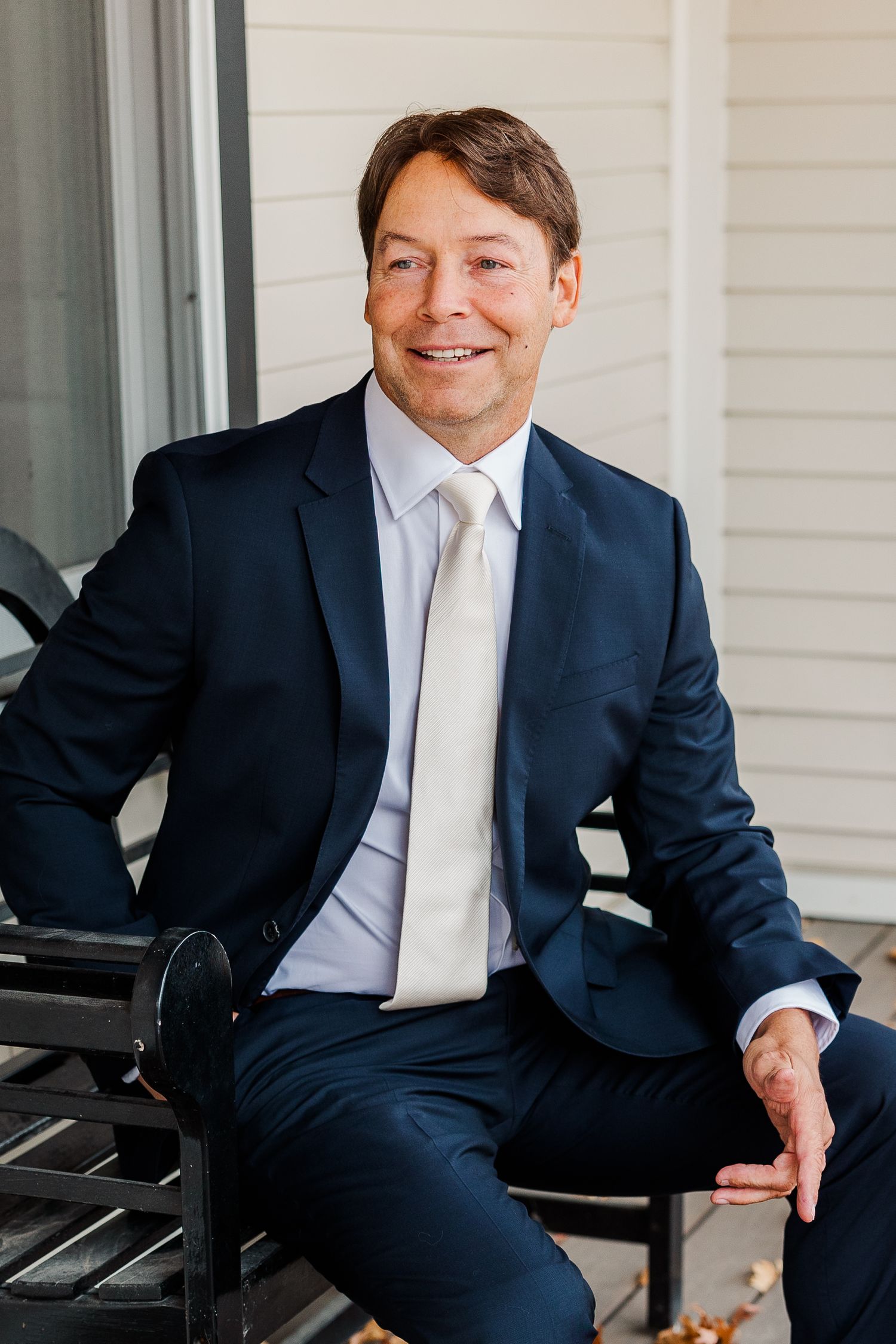 Professional portrait of a person in a navy suit seated outdoors.