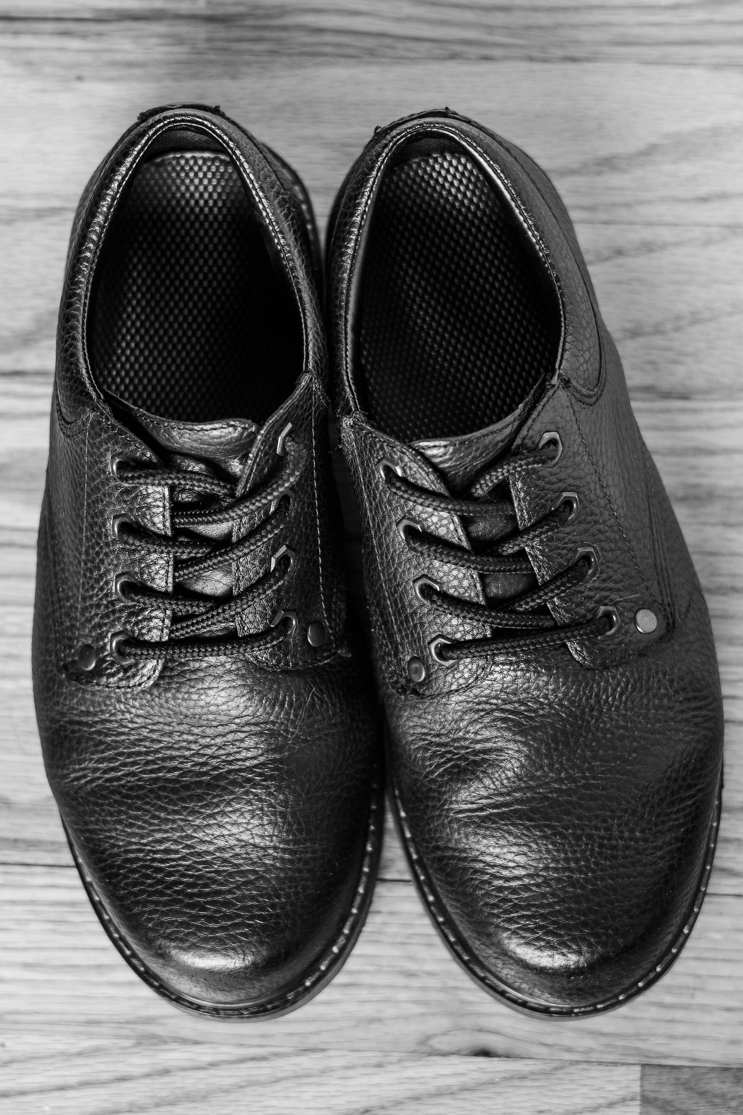 Black leather oxford dress shoes with textured surface on wooden floor.