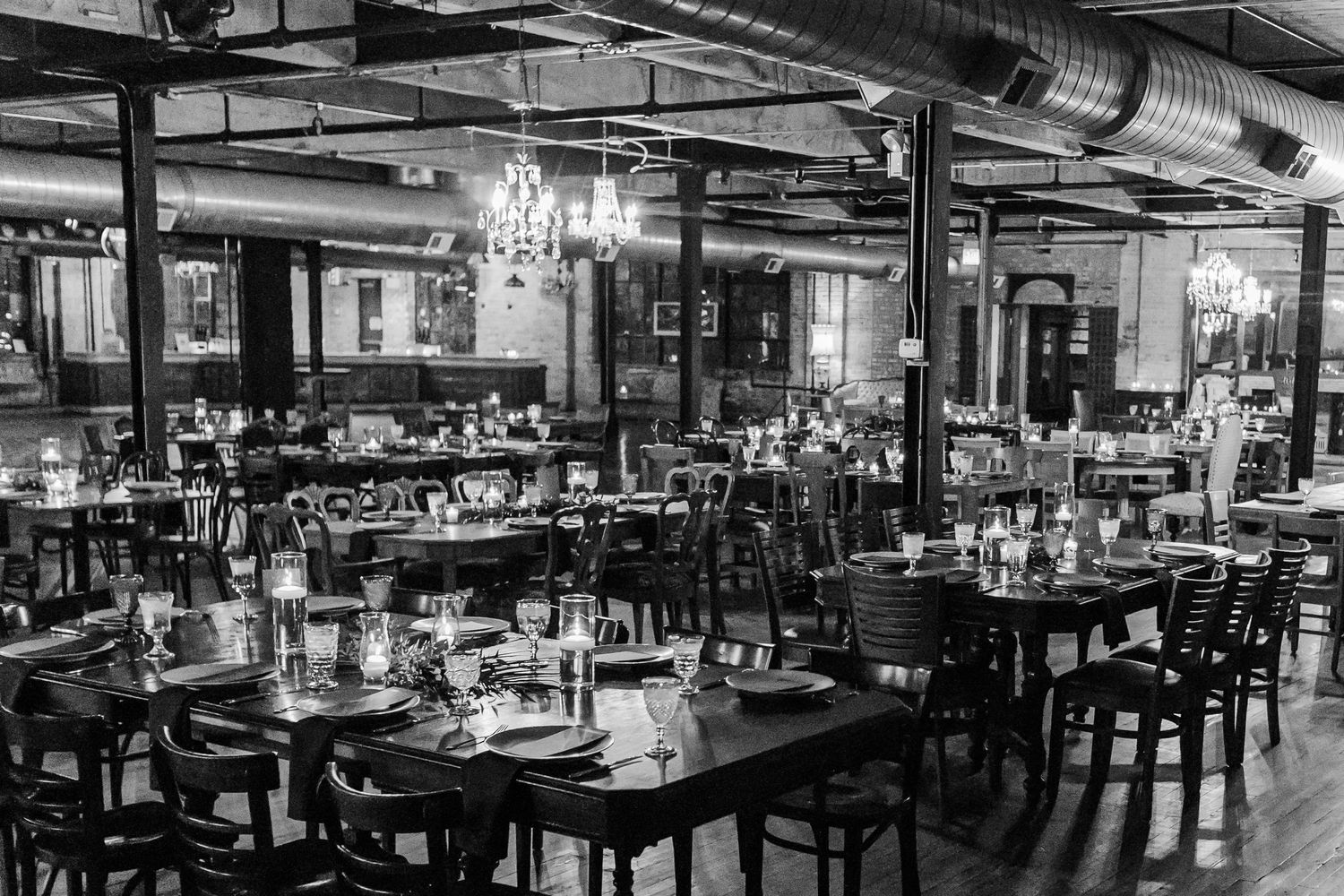Black and white photo of an industrial-style restaurant interior with elegant table settings.