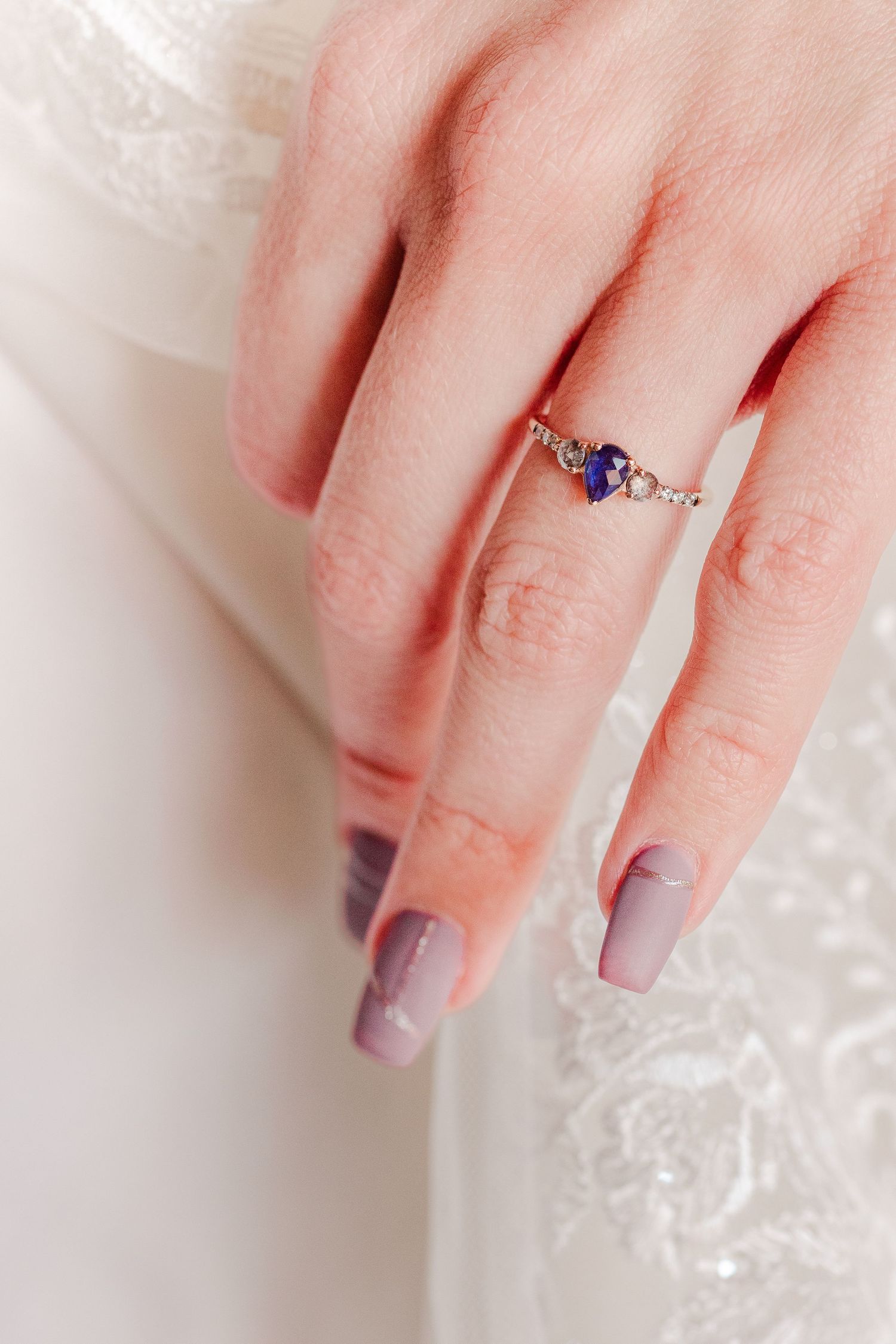 A delicate engagement ring with blue stones and small diamonds worn on a manicured hand.