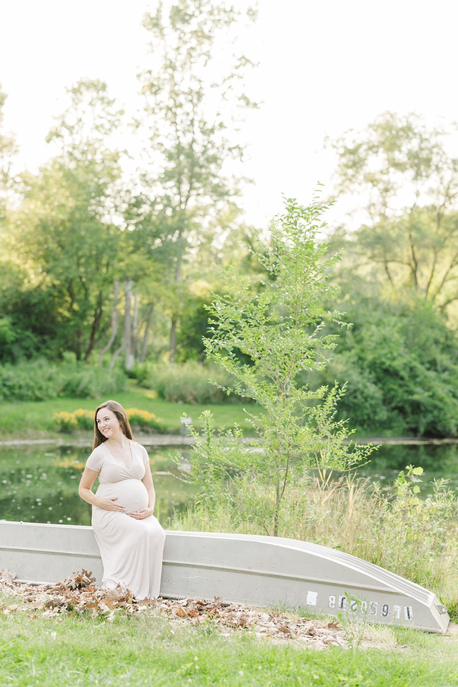 A couple relaxes on a concrete ledge near a tranquil pond surrounded by lush greenery on a bright summer day.