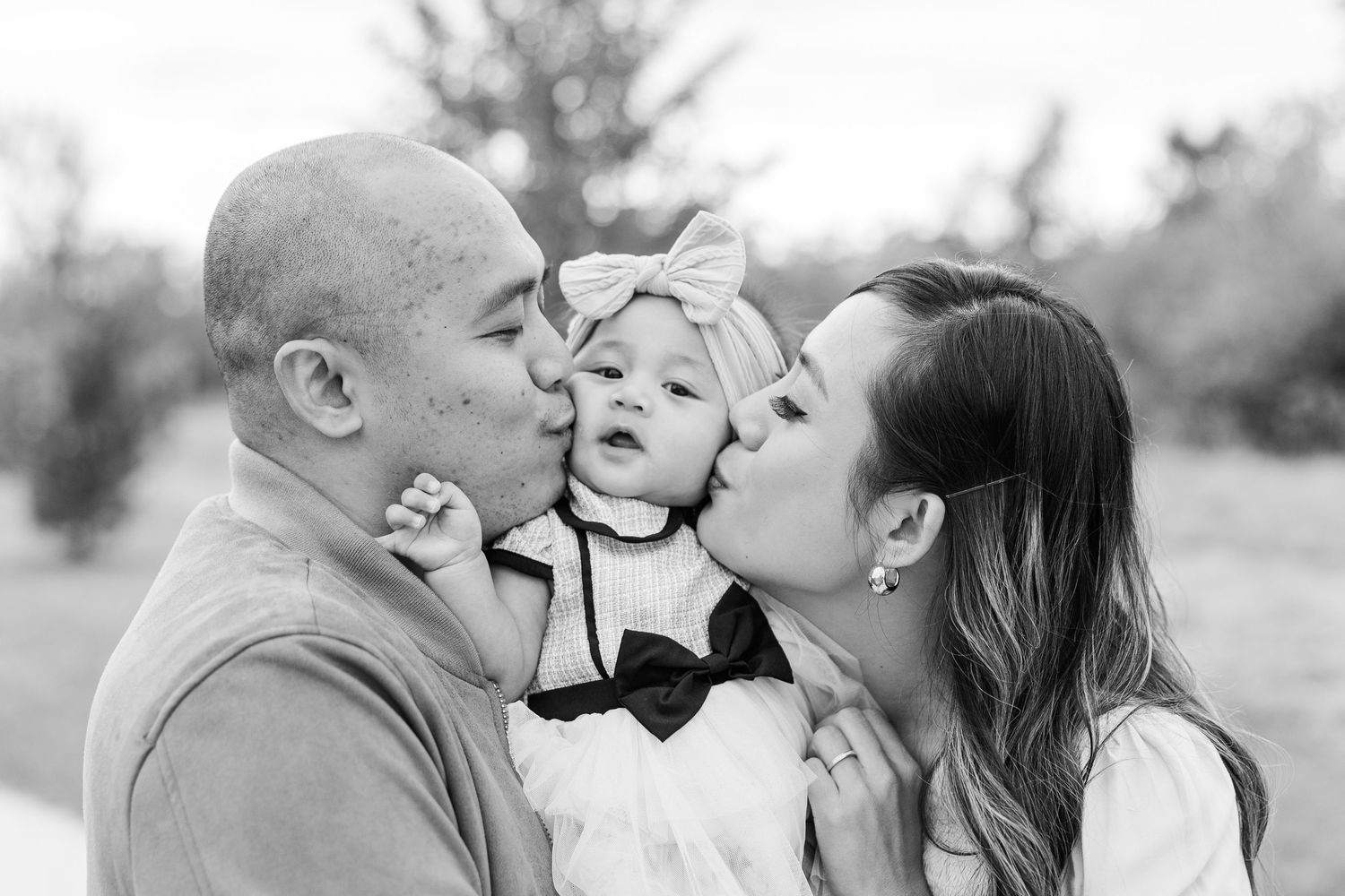 Black and white family portrait at a park in Prairie Grove, Illinois with parents kissing their baby girl