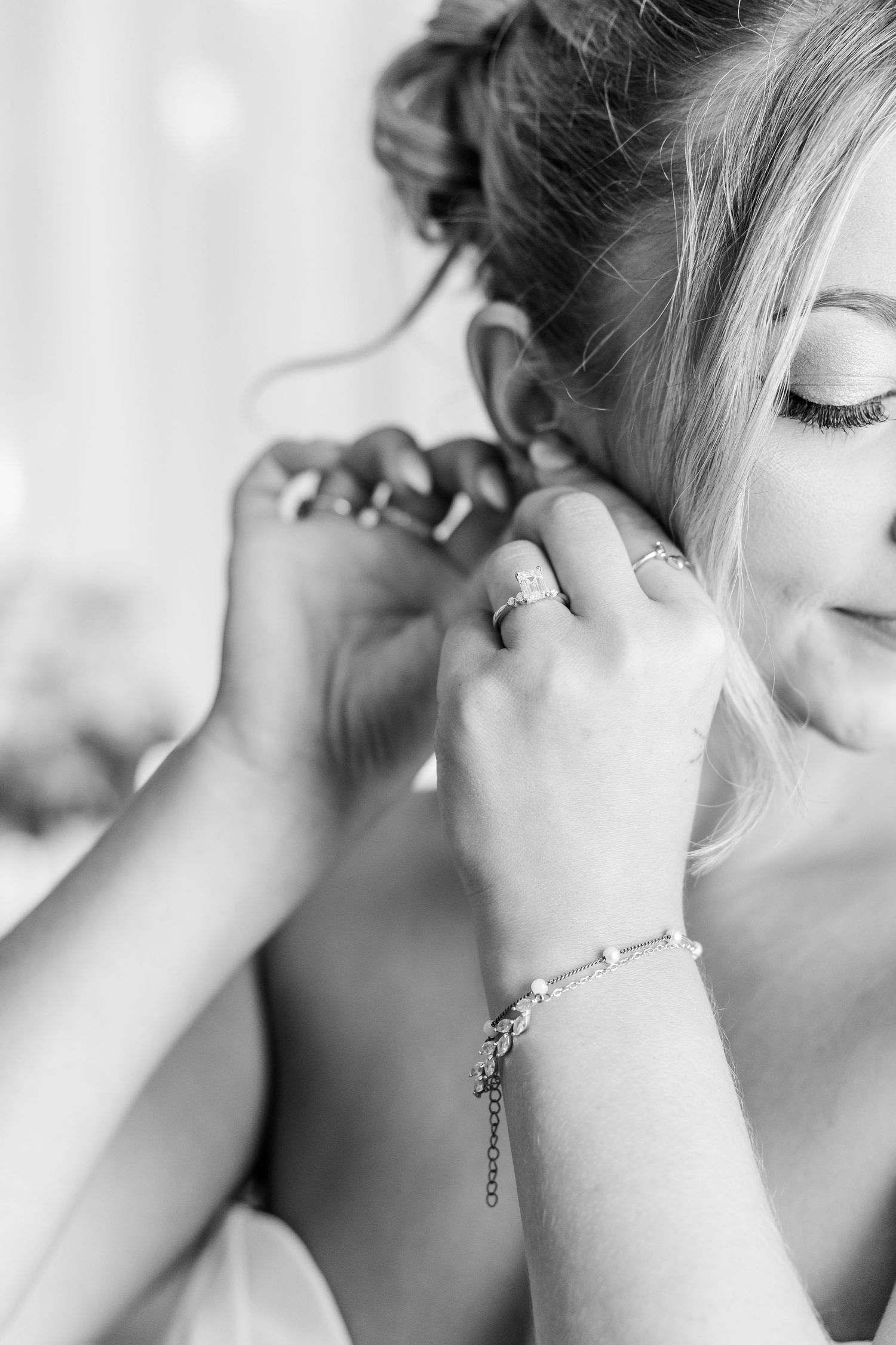 Black and white close-up of bride smiling as hands help her put on earrings and bracelet.