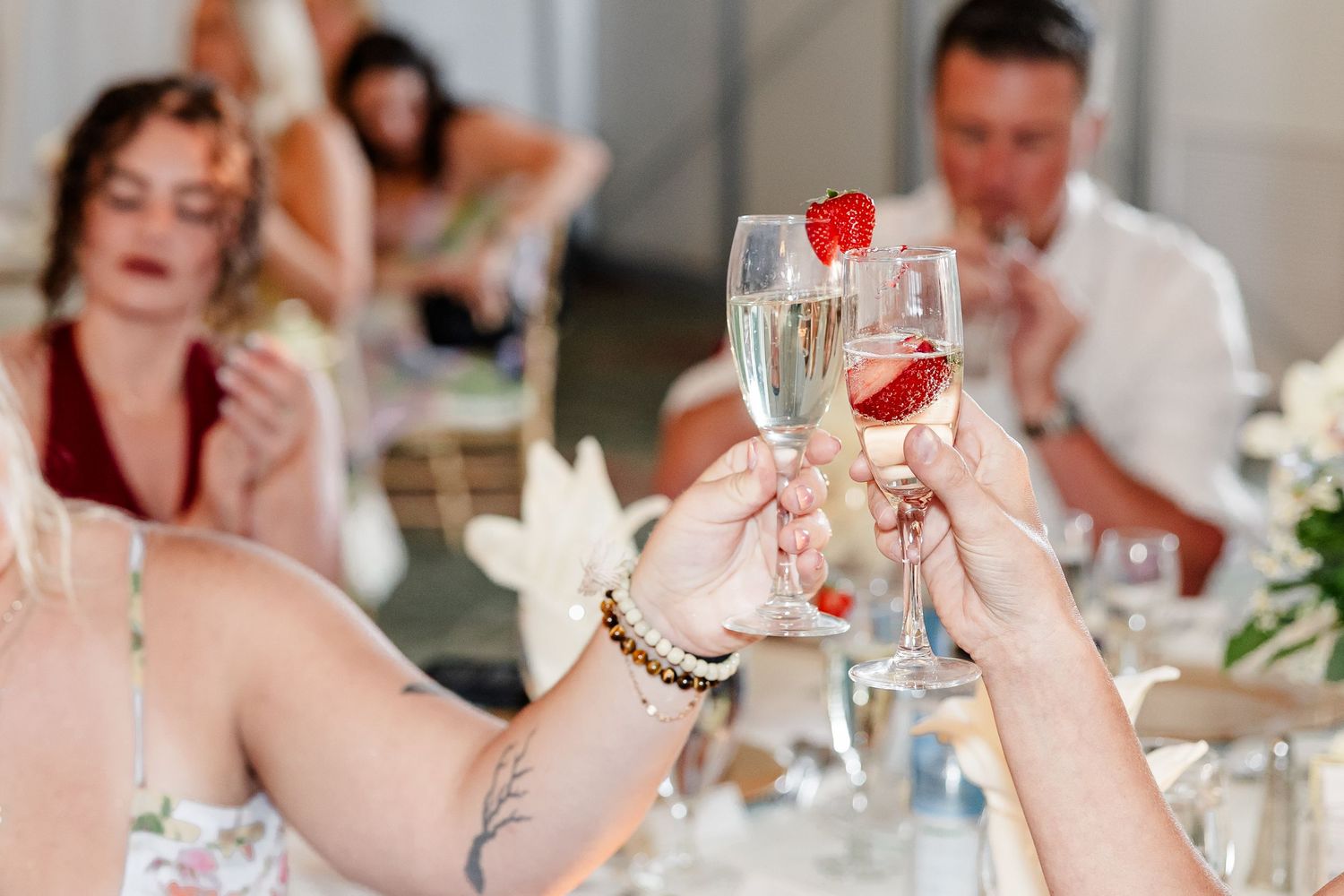 Two champagne flutes garnished with strawberries clink together in a toast at a wedding reception.
