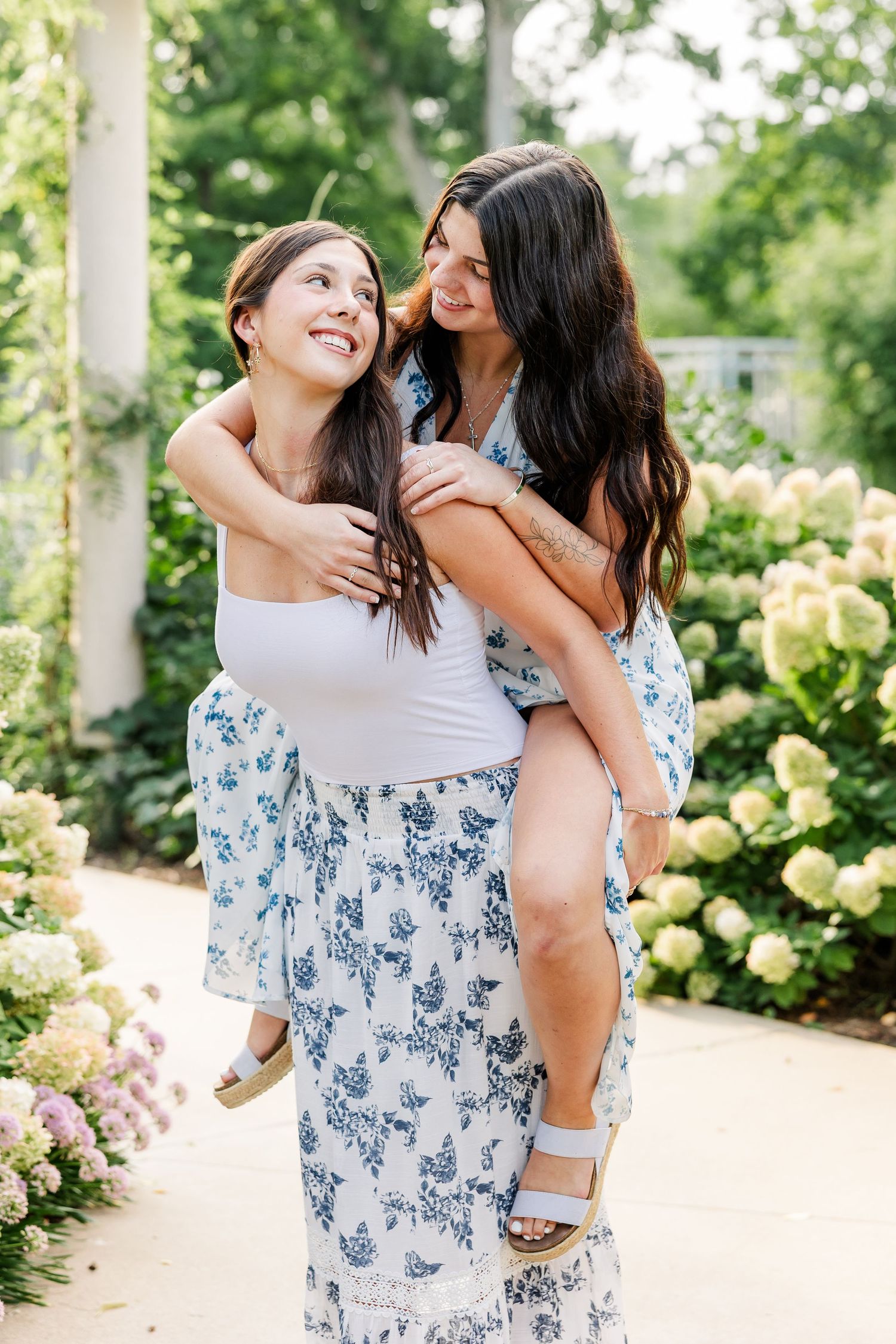Woman gives smiling girl a piggyback ride among blooming hydrangeas outdoors.