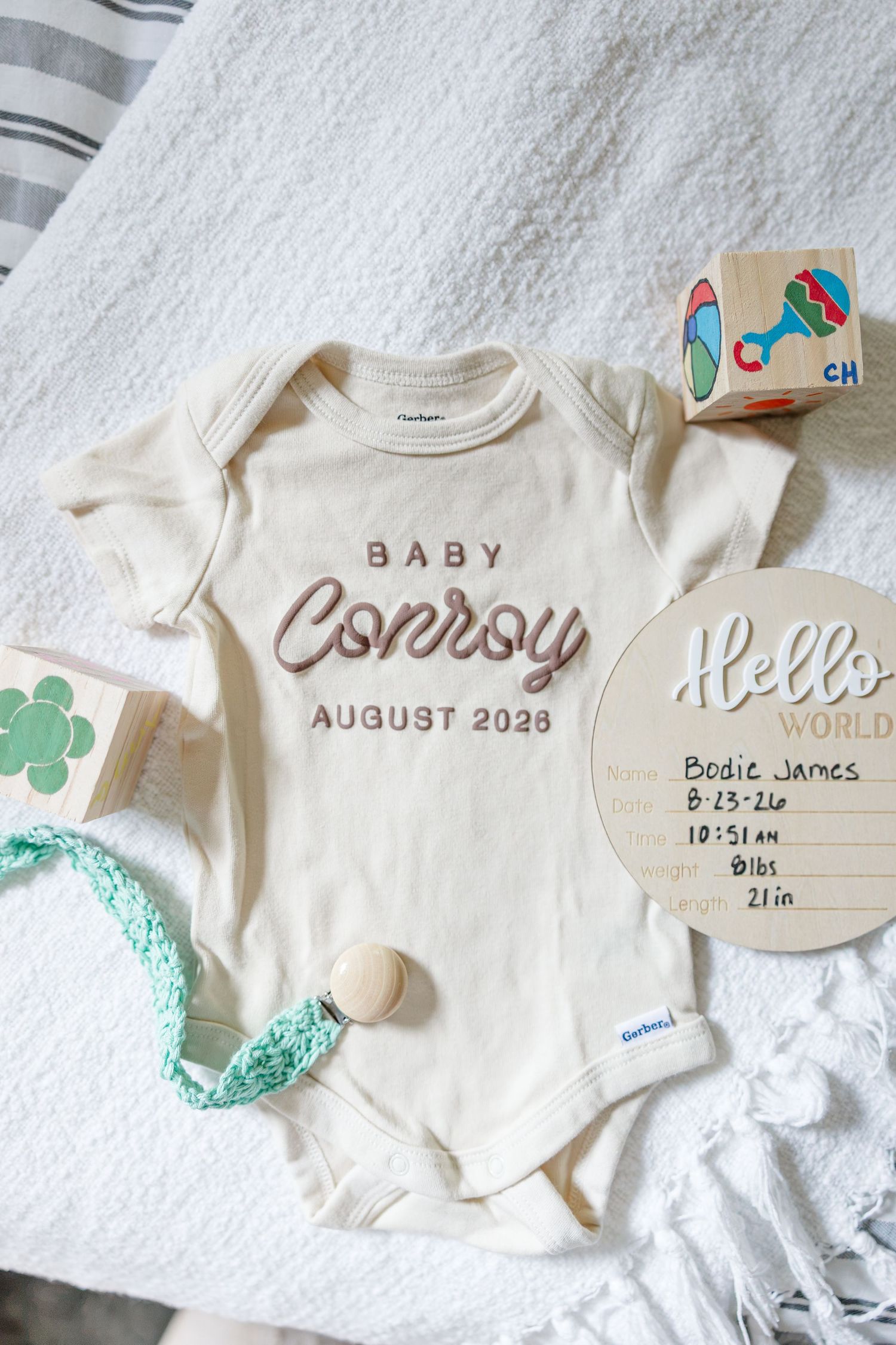 Baby Conroy August 2028 personalized onesie flatlay with Hello World birth stats sign and toys.
