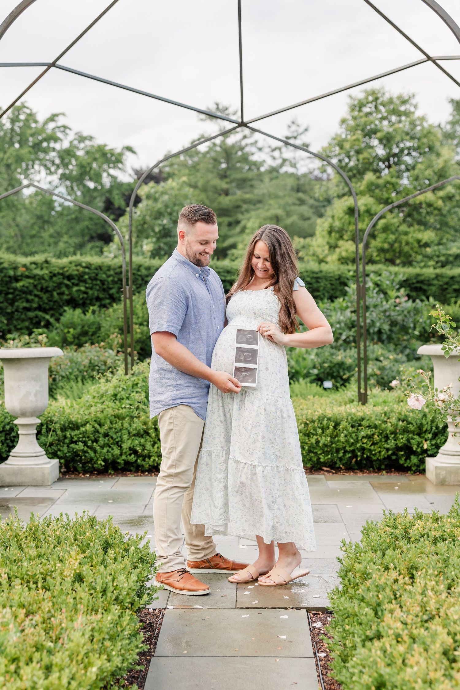Expecting parents holding an ultrasound under an umbrella during a garden maternity session