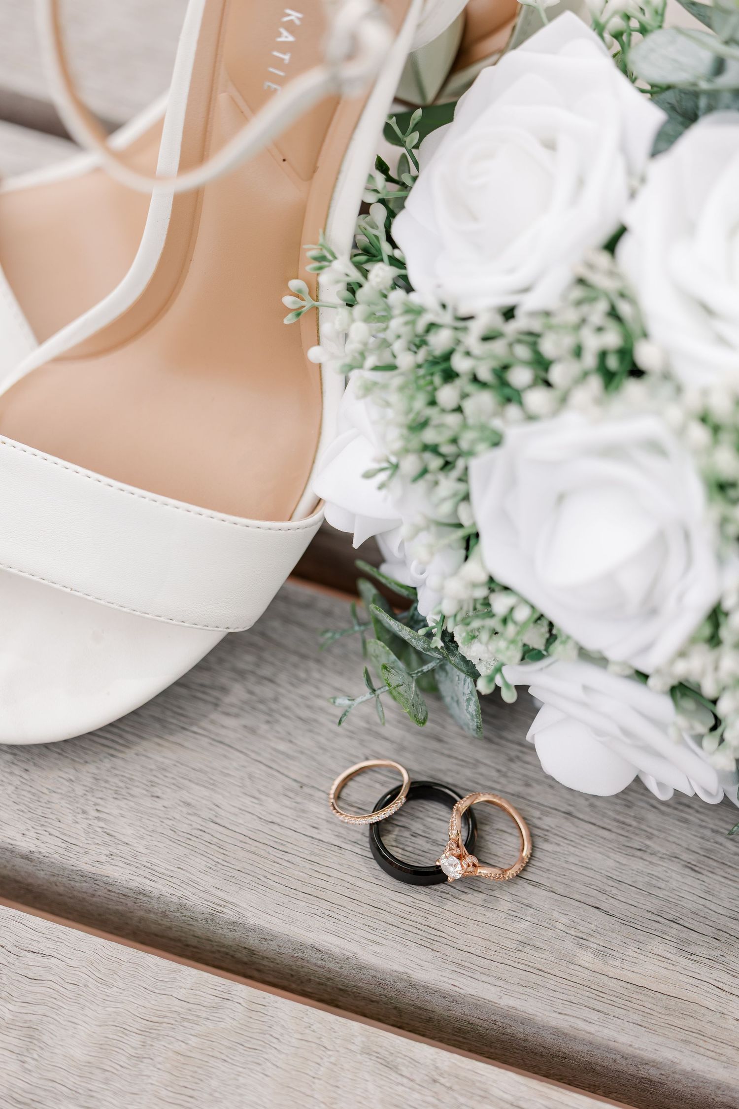 Wedding rings displayed beside Monika’s ivory shoes and white rose bouquet.