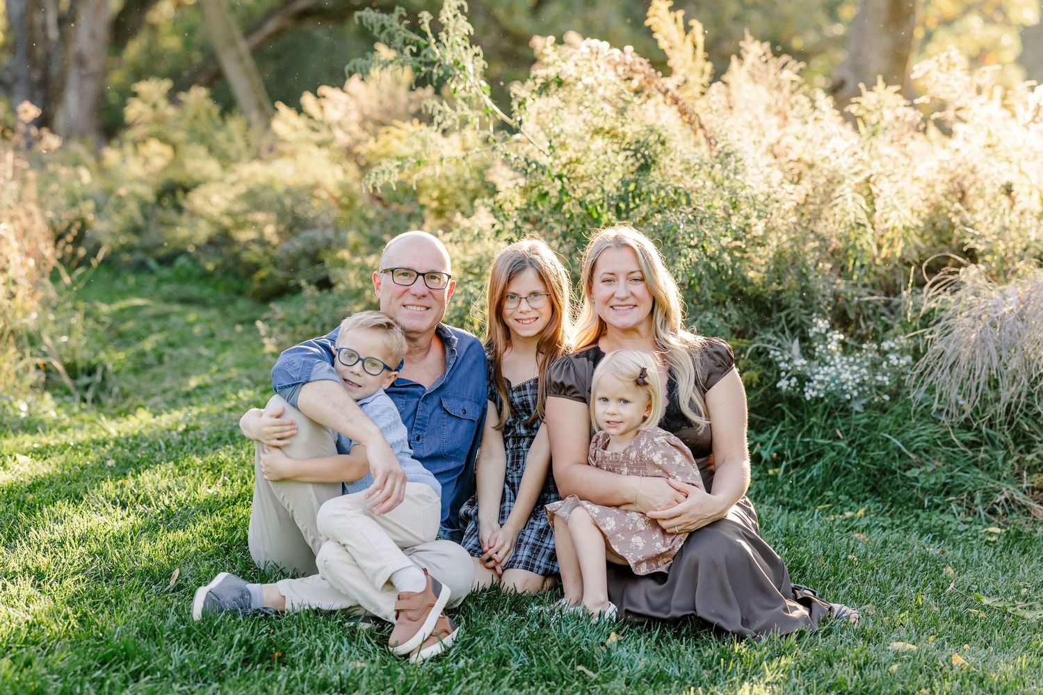 Family of five sitting together on a blanket in their sunlit backyard in St. Charles, IL.