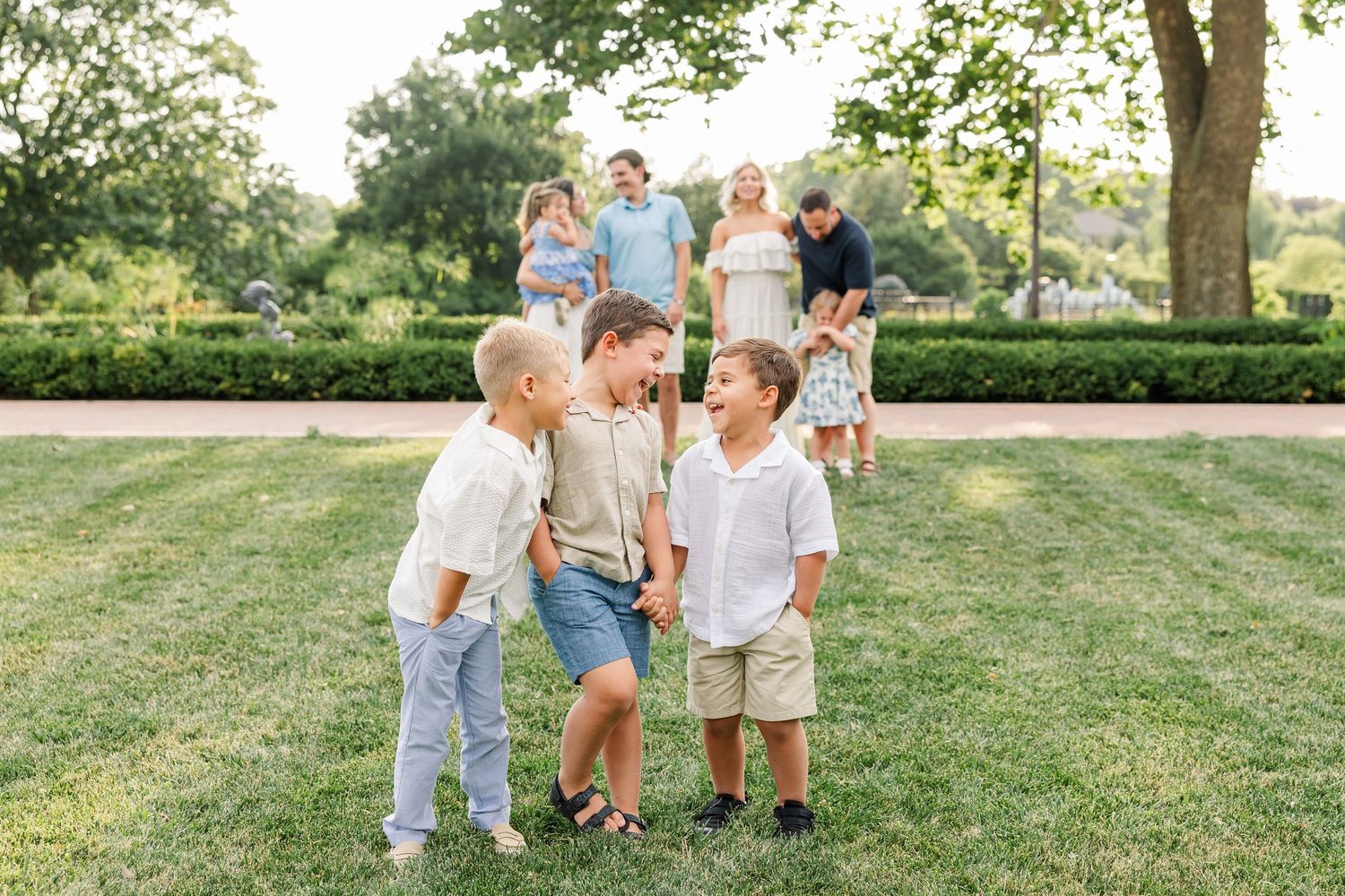 Family gathering outdoors on green lawn, two young boys playing in foreground, parents with children standing behind them.