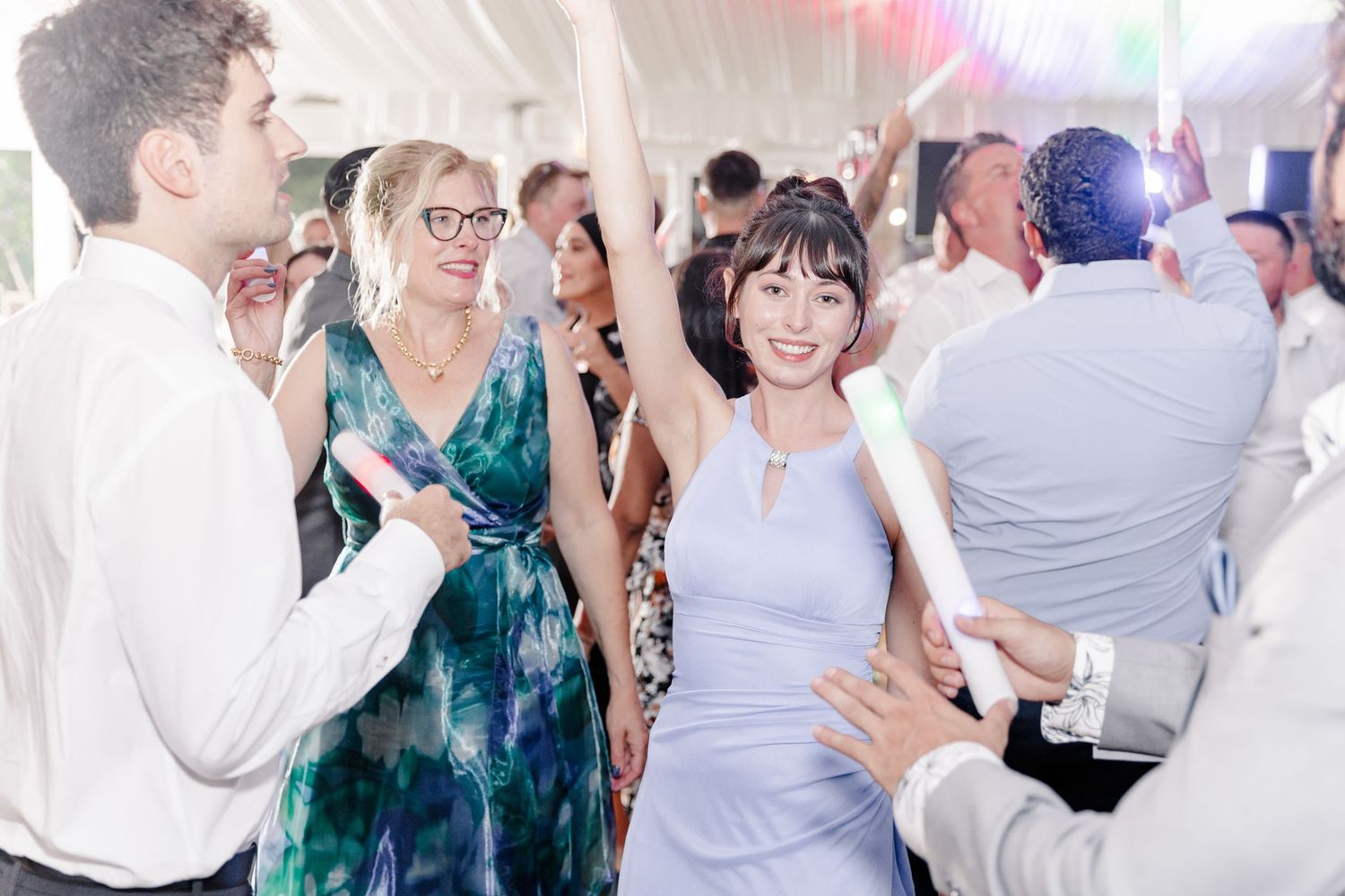 Guests dance and celebrate joyfully inside a bright white tent at a festive wedding reception.