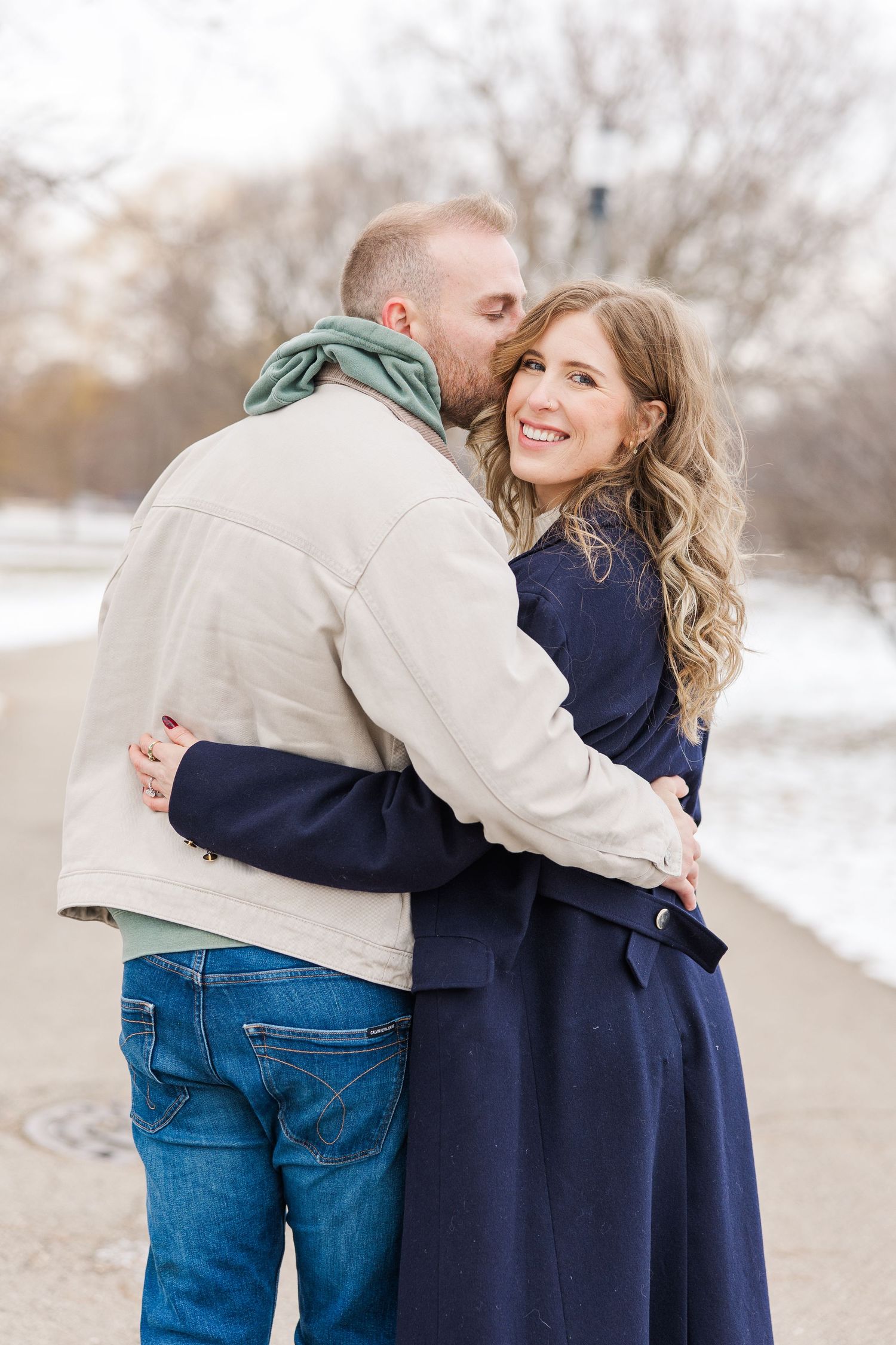 Romantic winter embrace between couple in navy and beige clothing against snowy outdoor backdrop. Winnemac park Chicago